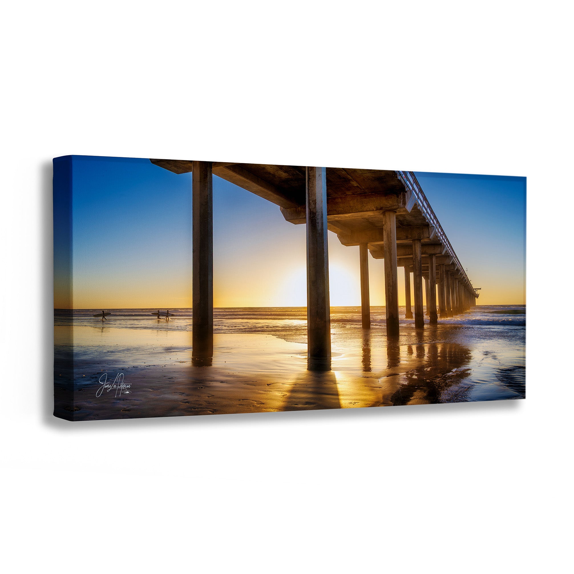 A rectangular canvas wall art print showing a pier over a beach at sunset, with blue sky, golden sunlight, and reflections in the wet sand. The canvas is photographed at a slight angle on a plain white background.