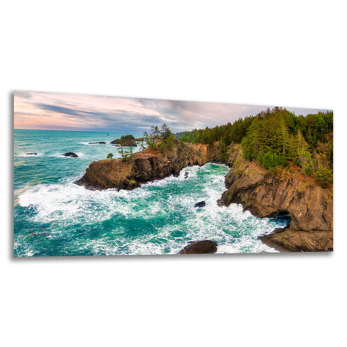 A panoramic landscape photo print of a rocky coastline with turquoise ocean waves crashing against brown cliffs and green trees under a cloudy sky, shown as a rectangular wall art piece on a white background.