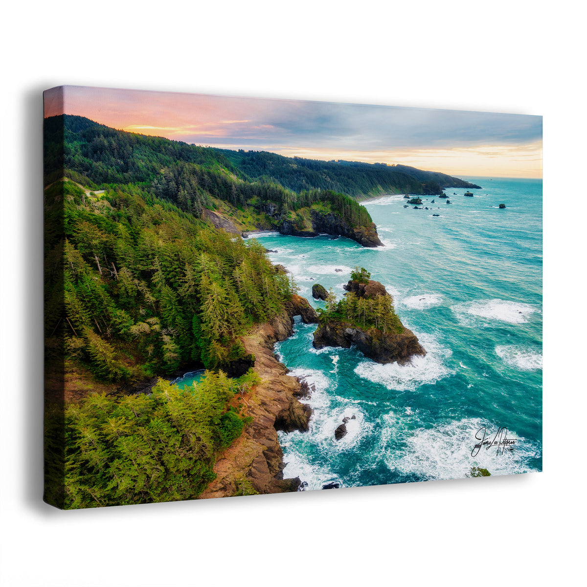 A canvas wall art print showing an aerial coastal landscape with dense green forested cliffs, rocky shoreline, turquoise ocean water, and a cloudy sunset sky. The canvas is photographed at an angle against a plain white background.