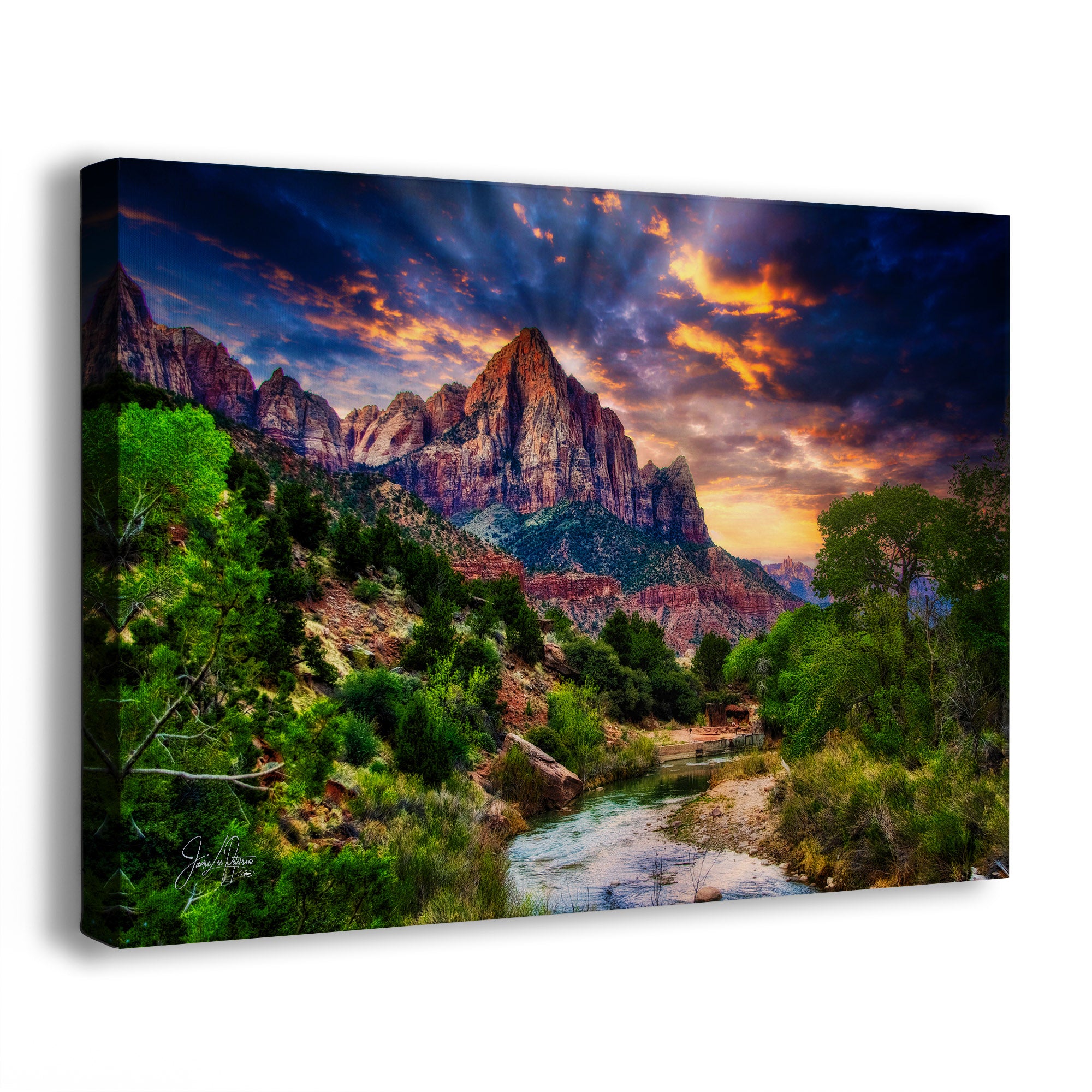 A rectangular canvas wall art print depicting a dramatic sunrise over Watchman Mountain in Zion National Park, with a river in the foreground, photographed at an angle against a plain white background.