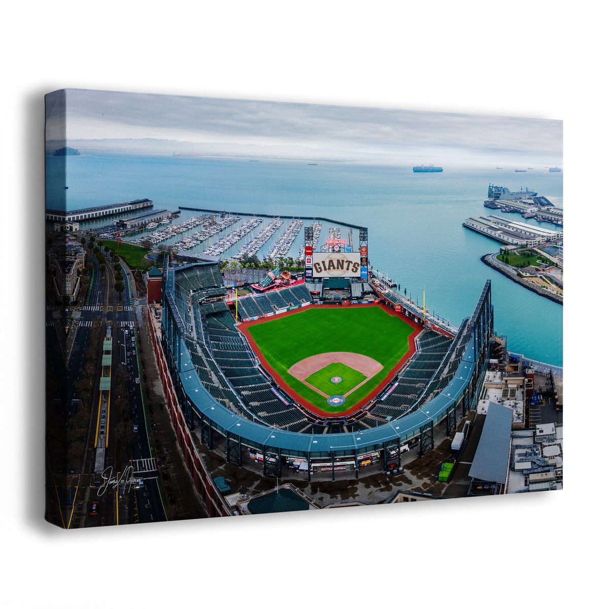 An Oracle Park Marina wall art print showing an aerial view of the San Francisco Giants' baseball stadium by the water, with the stadium field in green and red and the surrounding harbor and boats. The print is photographed at an angle against a plain white background.