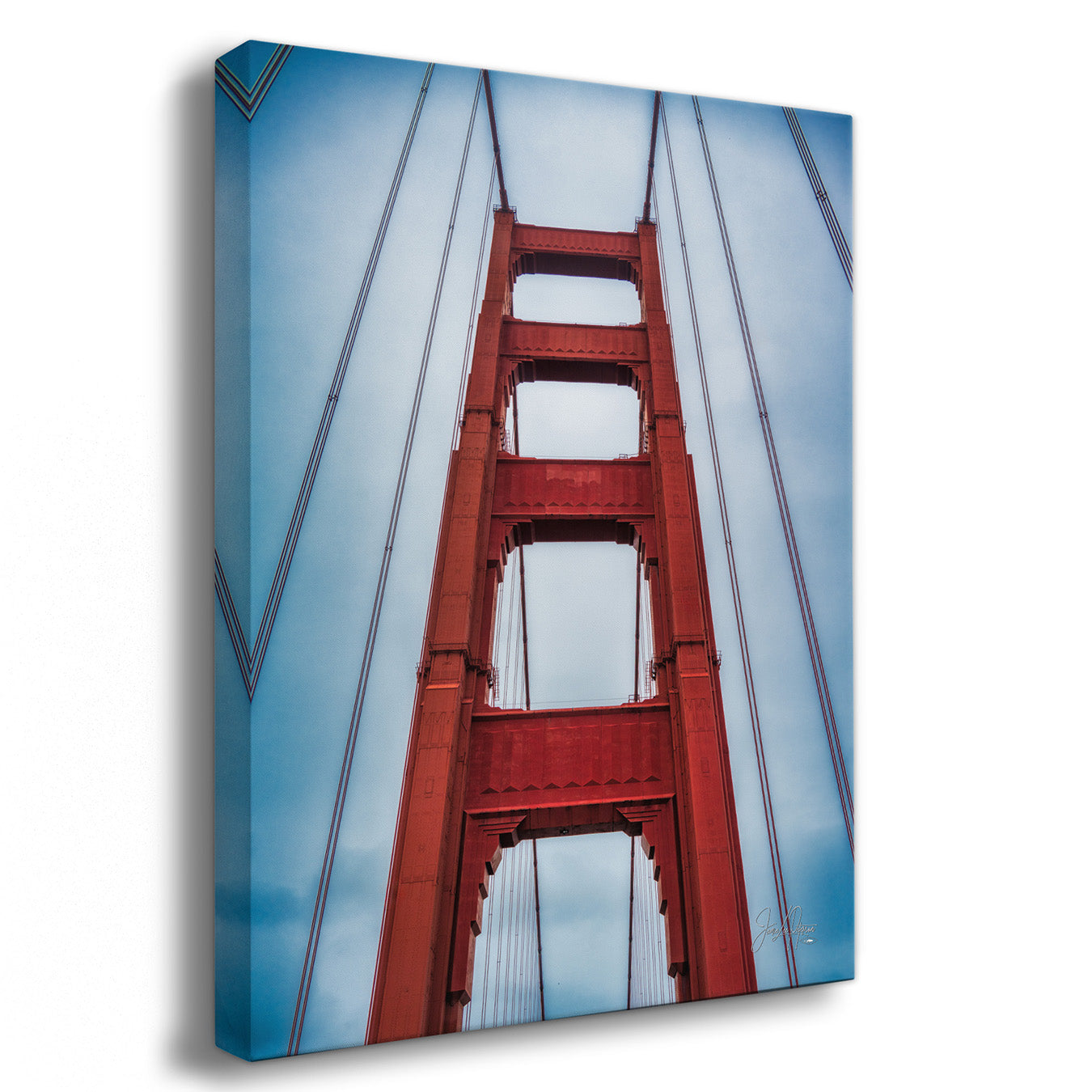 A square gallery-wrapped canvas print featuring a low-angle photograph of the Golden Gate Bridge against a blue sky, shown at a three-quarter angle on a white background.
