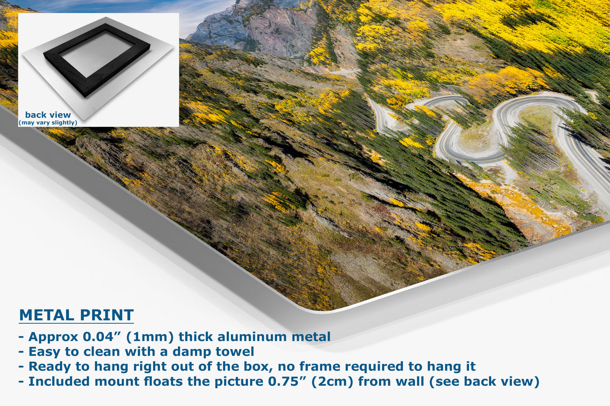 Corner view of an aluminum metal wall art print showing a winding mountain road through yellow autumn foliage, presented at an angle with product details and text on a white background. An inset shows the back view of the frame.