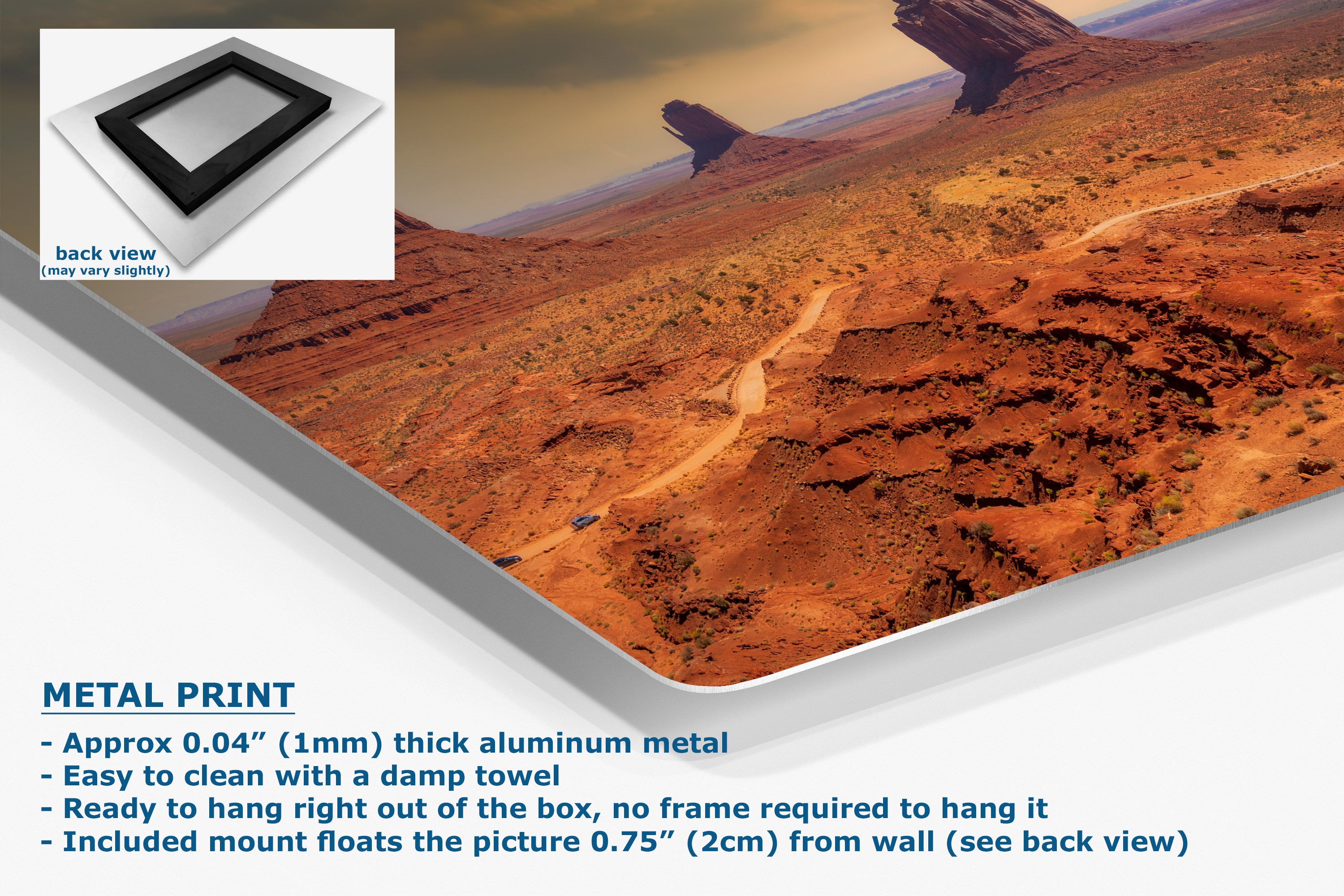 A corner view of a metal wall art print showing an aerial desert landscape with reddish-brown rock formations and a winding road, presented at an angle with a small inset showing the back view. Text on the image describes the product.