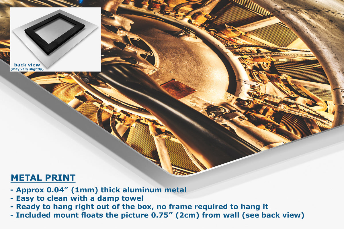 A corner view of an aluminum metal wall art print showing a close-up industrial mechanical scene in warm metallic tones, presented at an angle with product text and a small back-view inset on a white background.