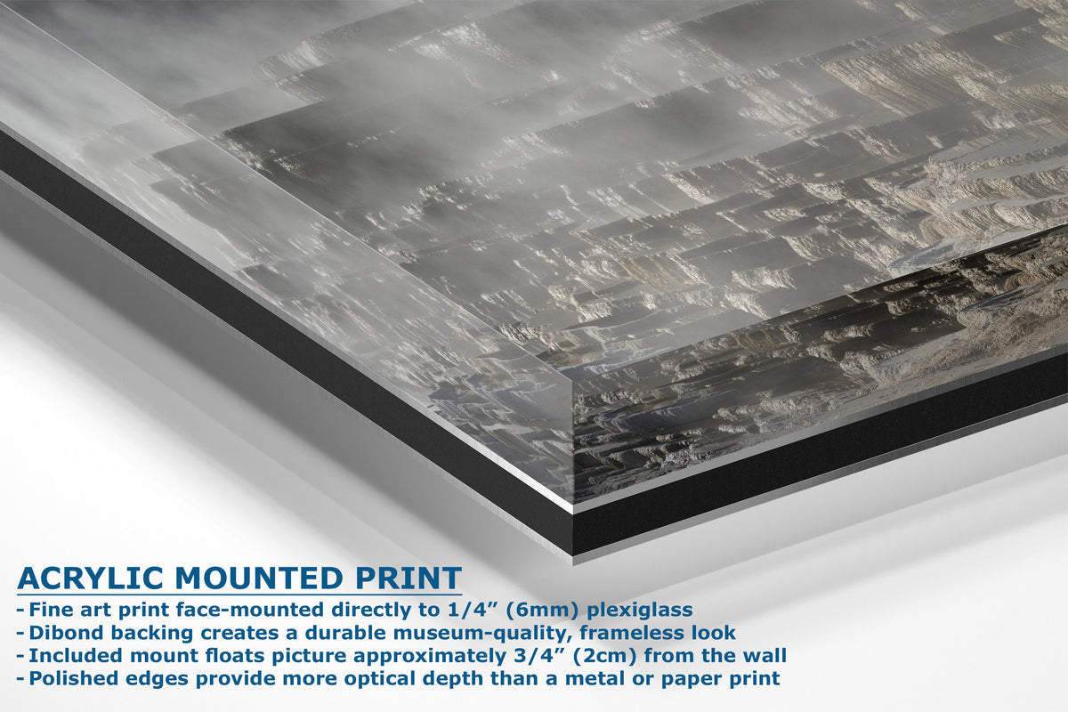 A corner view of an acrylic mounted art print showing a close-up of a textured gray and black abstract print on a plexiglass panel, with descriptive text overlay detailing the mounting features.