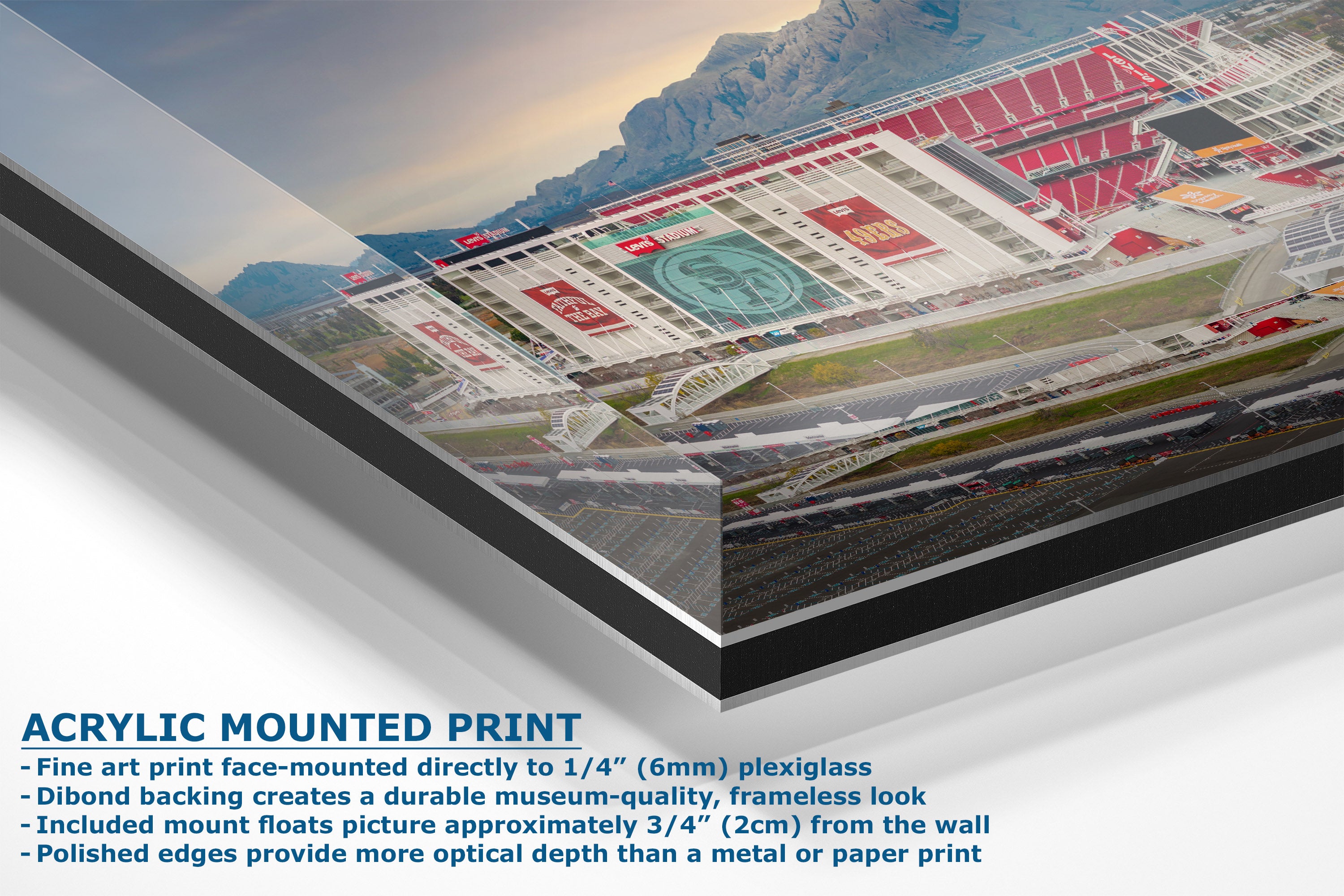 A corner view of an acrylic-mounted print of a stadium scene with red seating, green turf, and mountains in the background, shown at an angle with product text overlay on a white background.