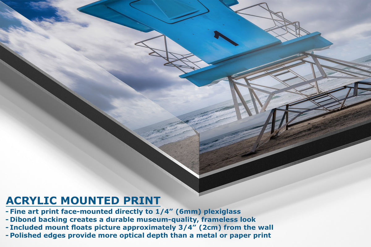Acrylic mounted art print of a beach scene with a bright blue lifeguard chair, shown at an angle with descriptive text on a white background.