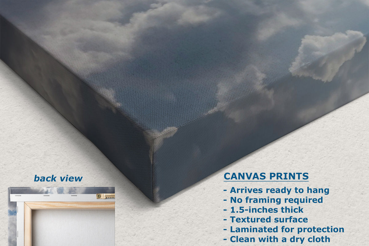 A corner view of a canvas wall art showing a cloudy sky scene, displayed at an angle with a textured off-white background. Text on the image includes 'CANVAS PRINTS' with features and a small inset labeled 'back view' showing the canvas edge.