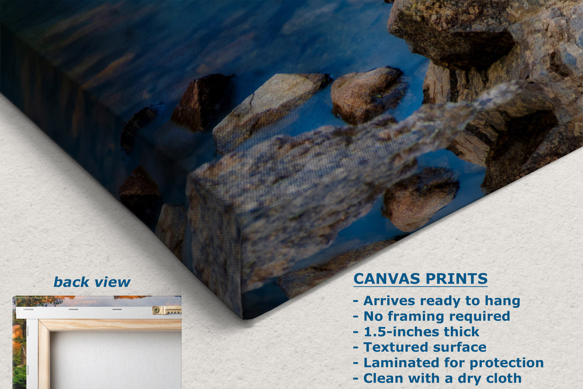 Canvas wall art print showing a rocky shoreline reflected in deep blue water, displayed at an angle with a small inset labeled back view and product text describing canvas print features.