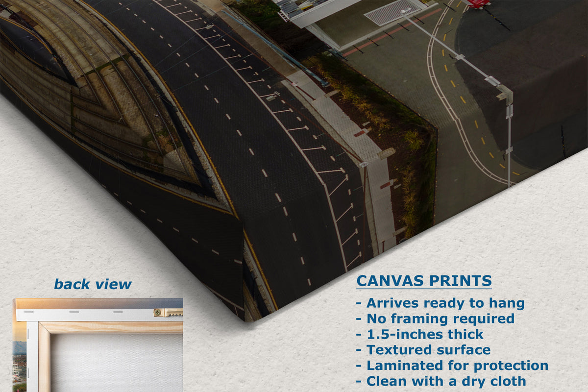 A corner view of a canvas wall art print shown at an angle with a textured surface, featuring a street scene with roads, buildings, and trees. The image includes text describing the print features and a small inset labeled back view showing a frame.