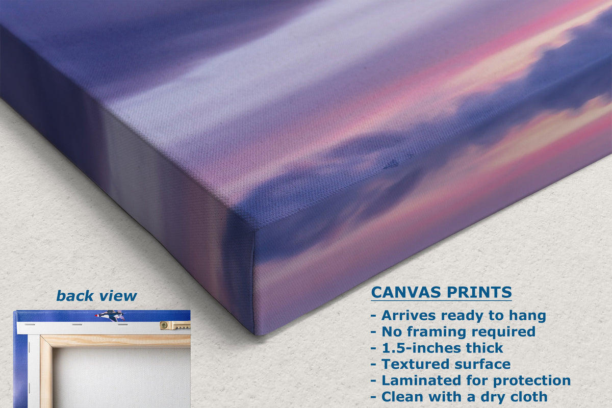 A corner view of a canvas print shown at an angle with a purple and pink sky design, on a light textured background. Text on the image describes the canvas print features, and a small inset shows the back view with a frame.