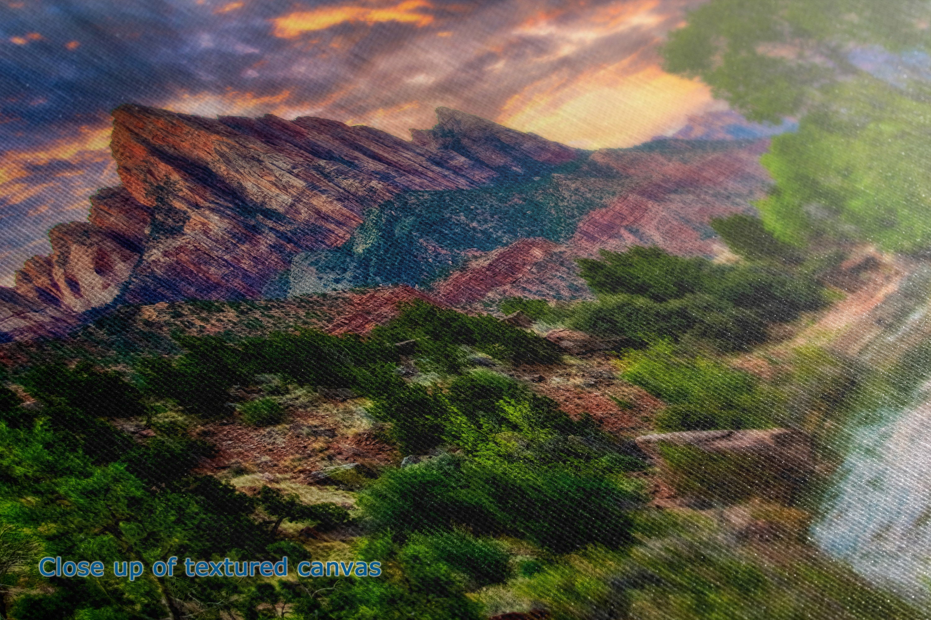 Close-up of a textured canvas print depicting a desert mountain landscape under a dramatic sunset sky with green trees in the foreground.
