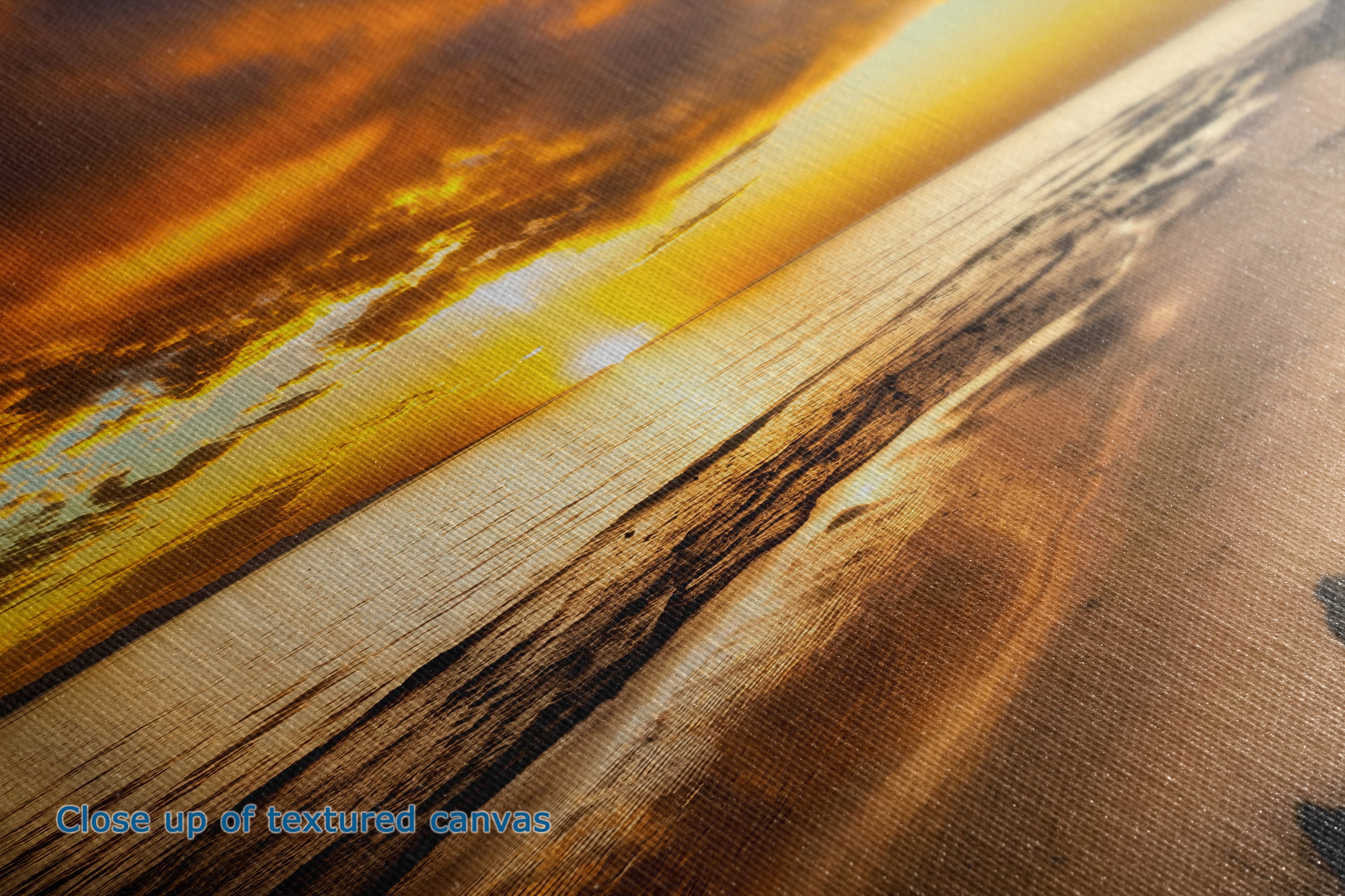 Close-up of a textured canvas print showing a dramatic sunset beach scene with golden yellow, orange, and brown tones.