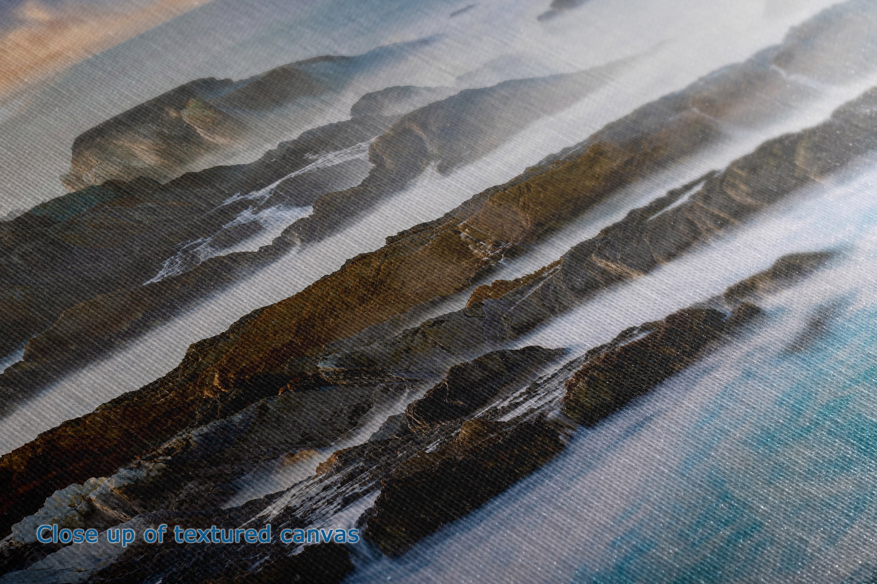 Close-up of a textured canvas print depicting a coastal landscape with dark rocky cliffs and blue water, with a blue text overlay reading 'Close up of textured canvas'.