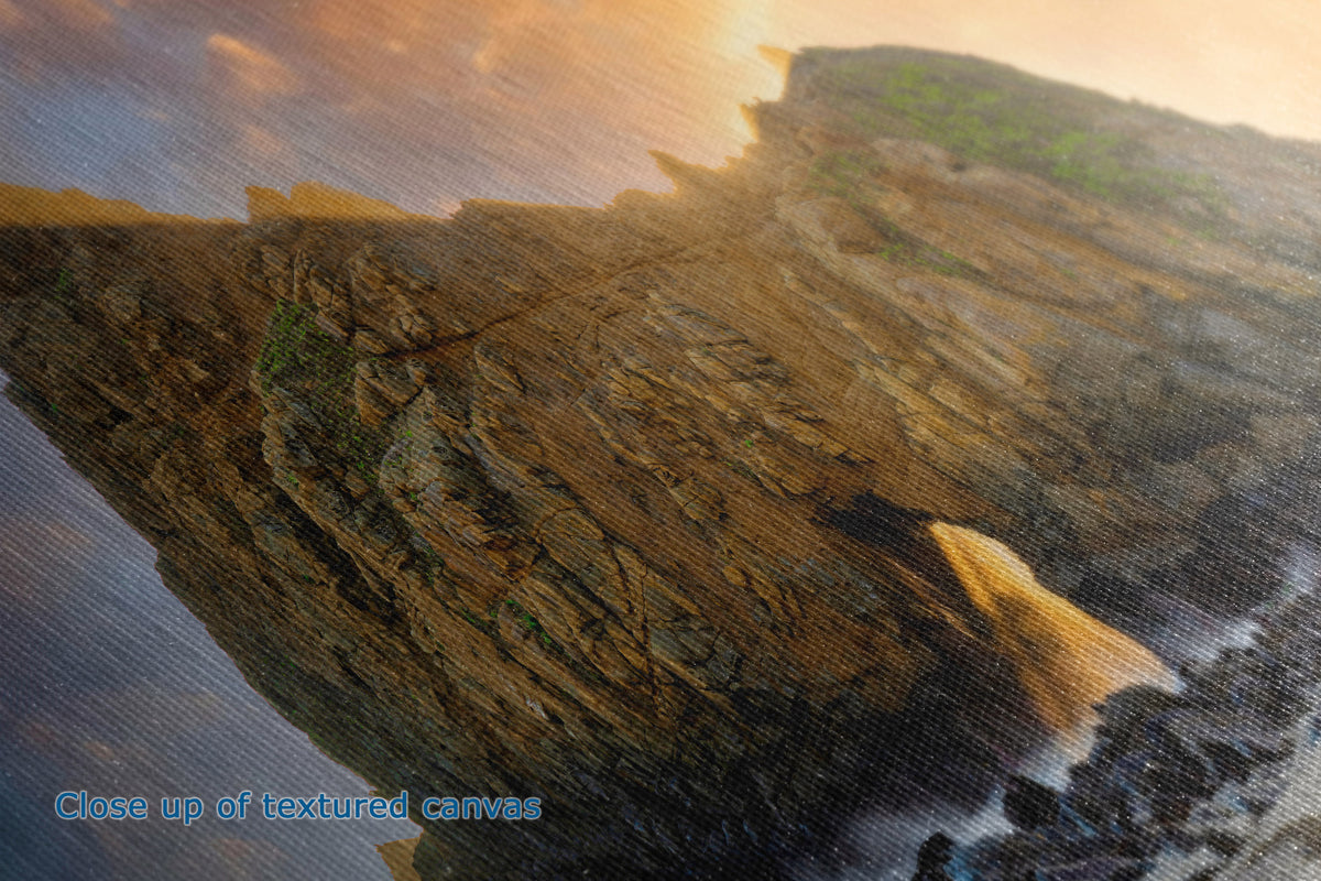 Close-up of a textured canvas print depicting a dramatic coastal cliffside scene at sunset, with warm golden light, dark rocky cliffs, and ocean waves below. Blue text in the lower-left corner reads 'Close up of textured canvas'.