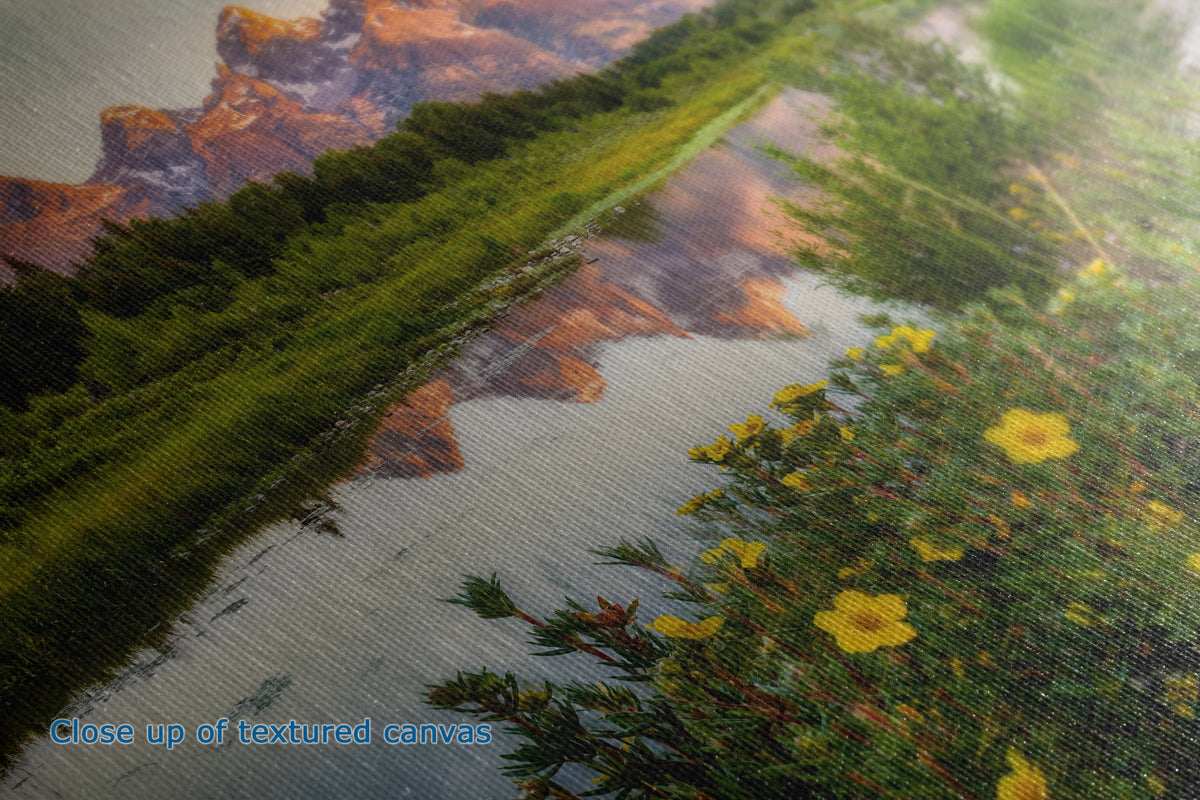 Close-up of a textured canvas print depicting a scenic landscape with a river, green trees, orange-brown cliffs, and yellow wildflowers. Blue text in the lower-left corner reads 'Close up of textured canvas'.