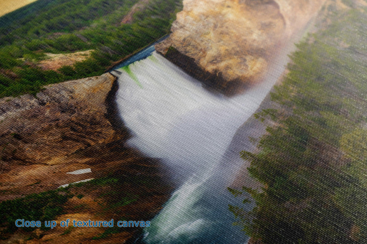 Close-up of a textured canvas print depicting a dramatic waterfall cascading down a rocky cliff into a river, surrounded by green forest.
