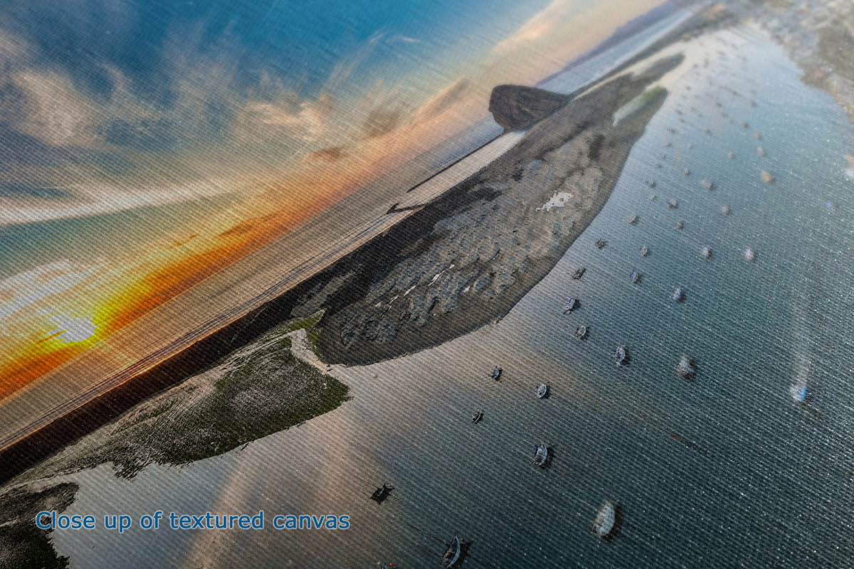 A close-up view of a textured canvas art print that shows an aerial view of a coastal landscape at sunset with a long shoreline, scattered boats on the water, and a textured sky in blue, orange, and gray tones.