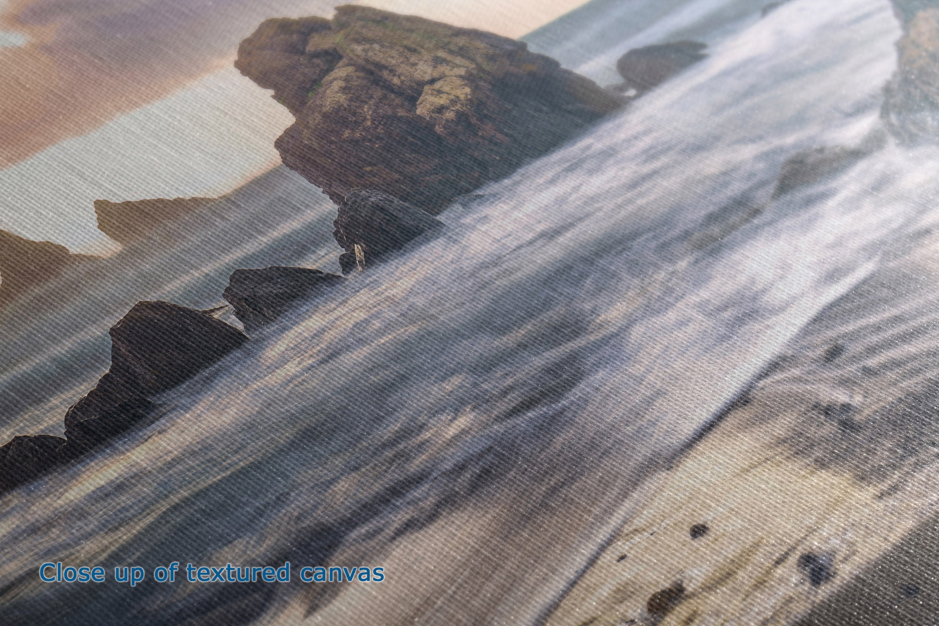 Close-up of a textured canvas print depicting a rocky coastline with waves, showing the fabric texture and printed details.