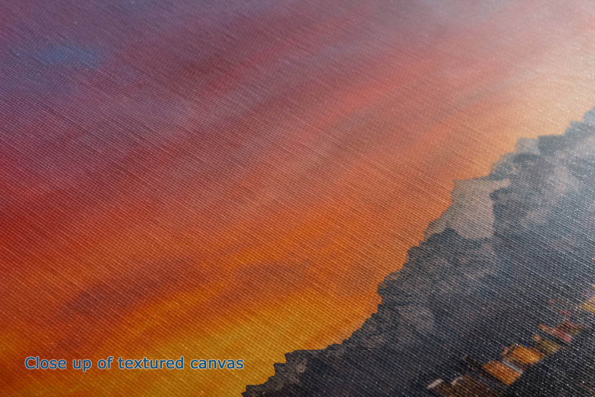 Close-up of a textured canvas painting showing a sunset sky gradient from deep red and orange to yellow, with a dark rocky shoreline along the bottom right.