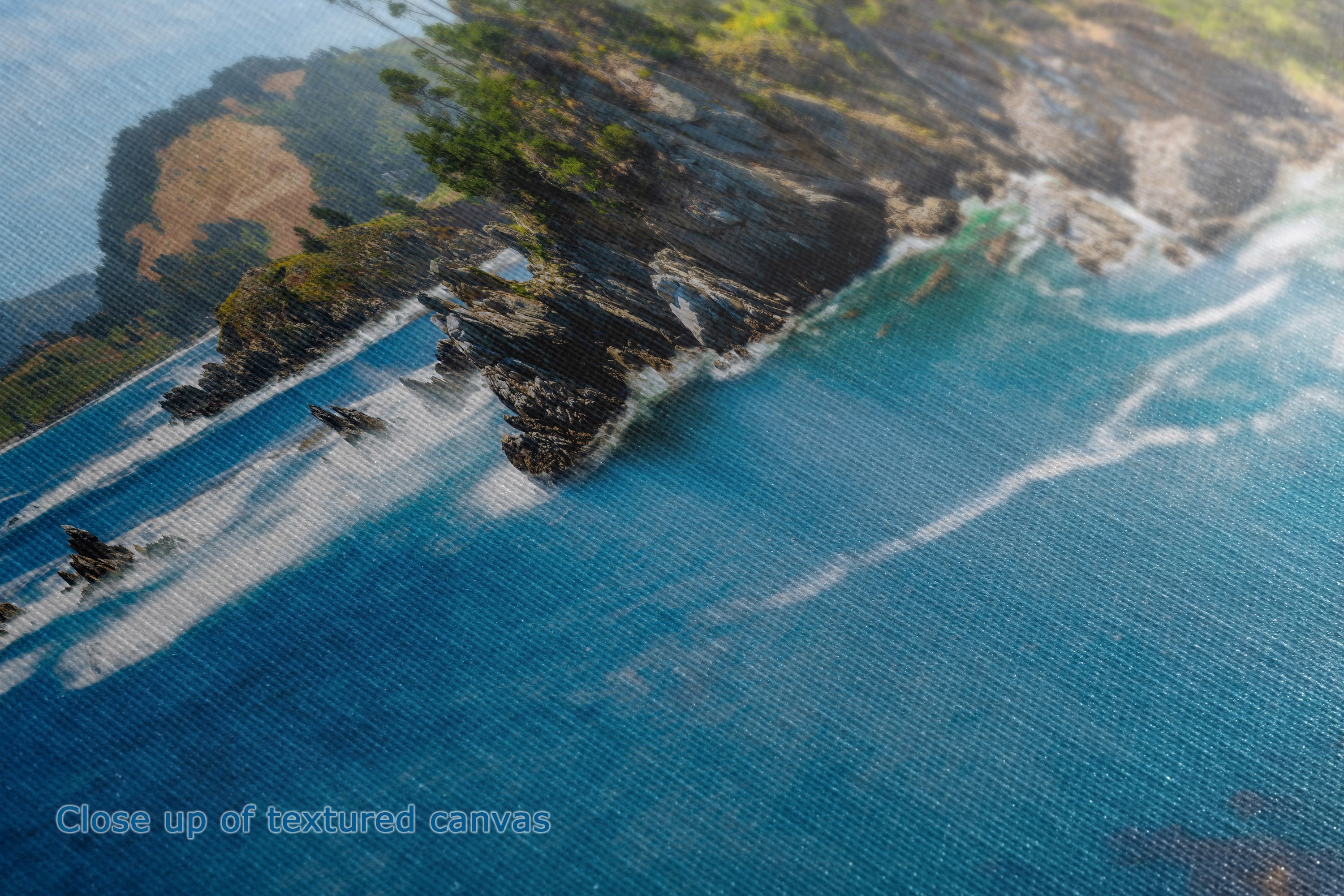 Close-up of a textured canvas print depicting a coastal landscape with blue ocean water, rocky shoreline, and green vegetation.