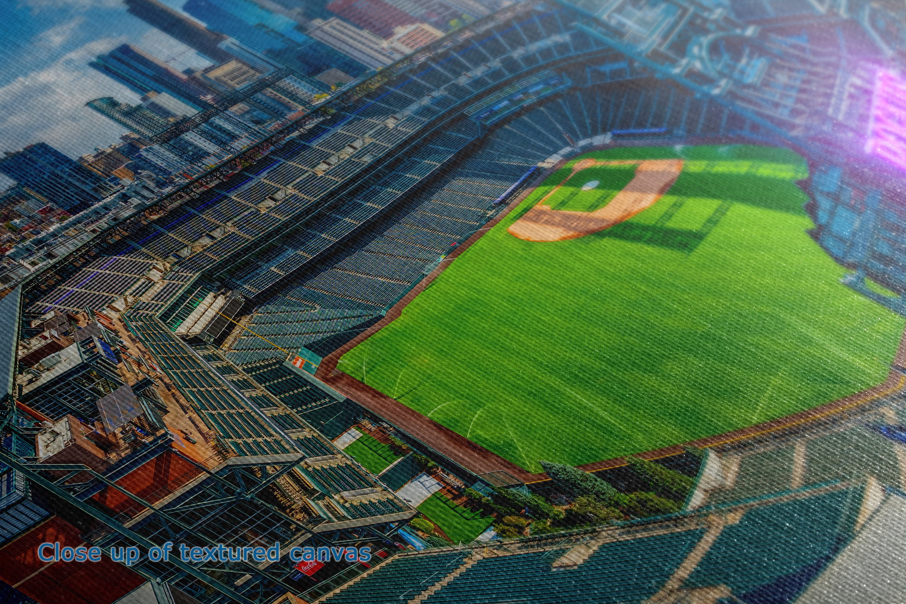 A close-up of the detail and texture of a canvas wall art print depicting an aerial view of a baseball stadium with a vibrant green field, surrounded by blue and gray seating and city buildings.