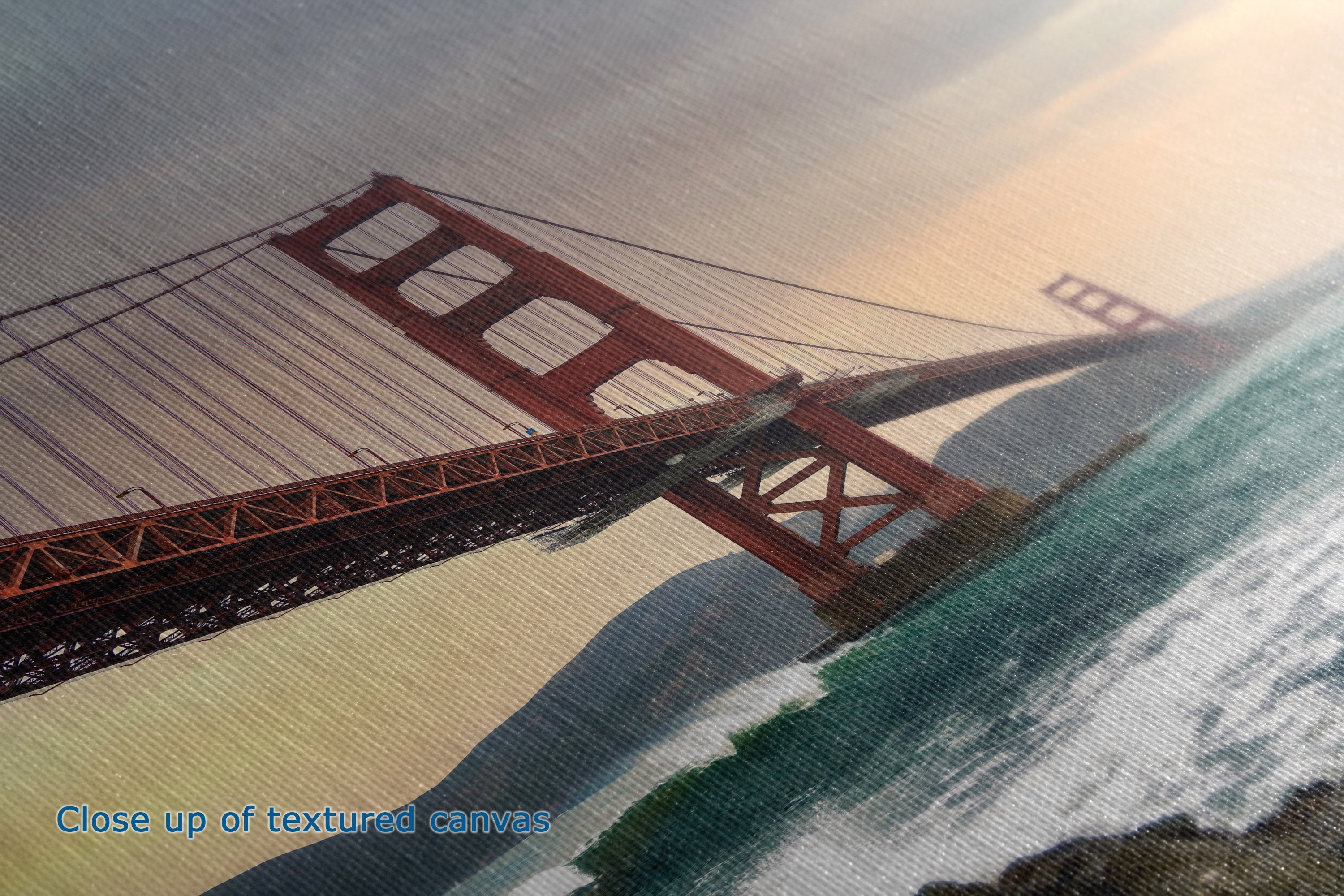 Close-up of a textured canvas print depicting the Golden Gate Bridge over water, with a blue text overlay reading 'Close up of textured canvas'.