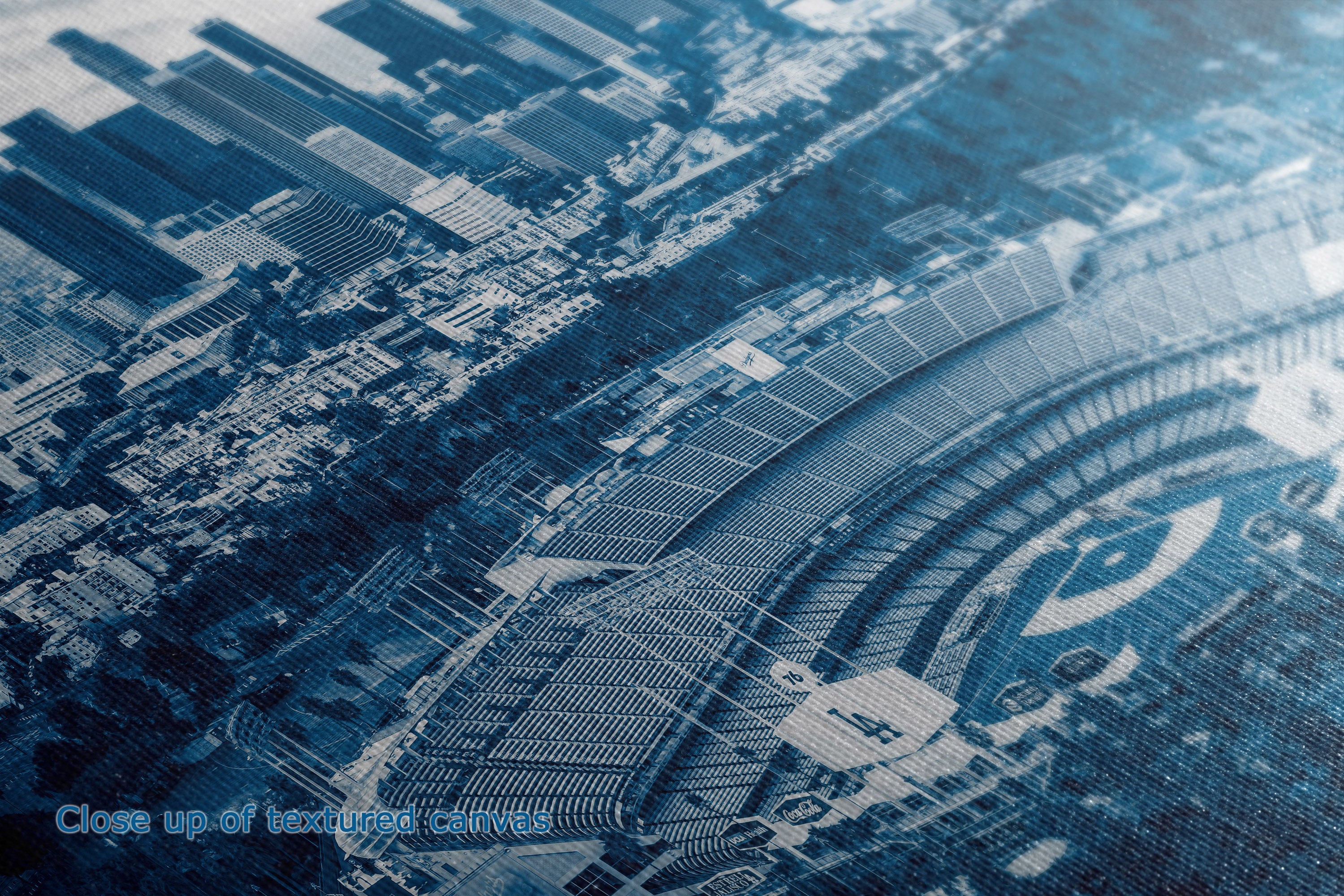 A close-up, angled view of a blue-toned printed graphic or artwork depicting a stadium and surrounding urban structures, with a small caption in the lower left reading 'Close up of printed cloth.'.