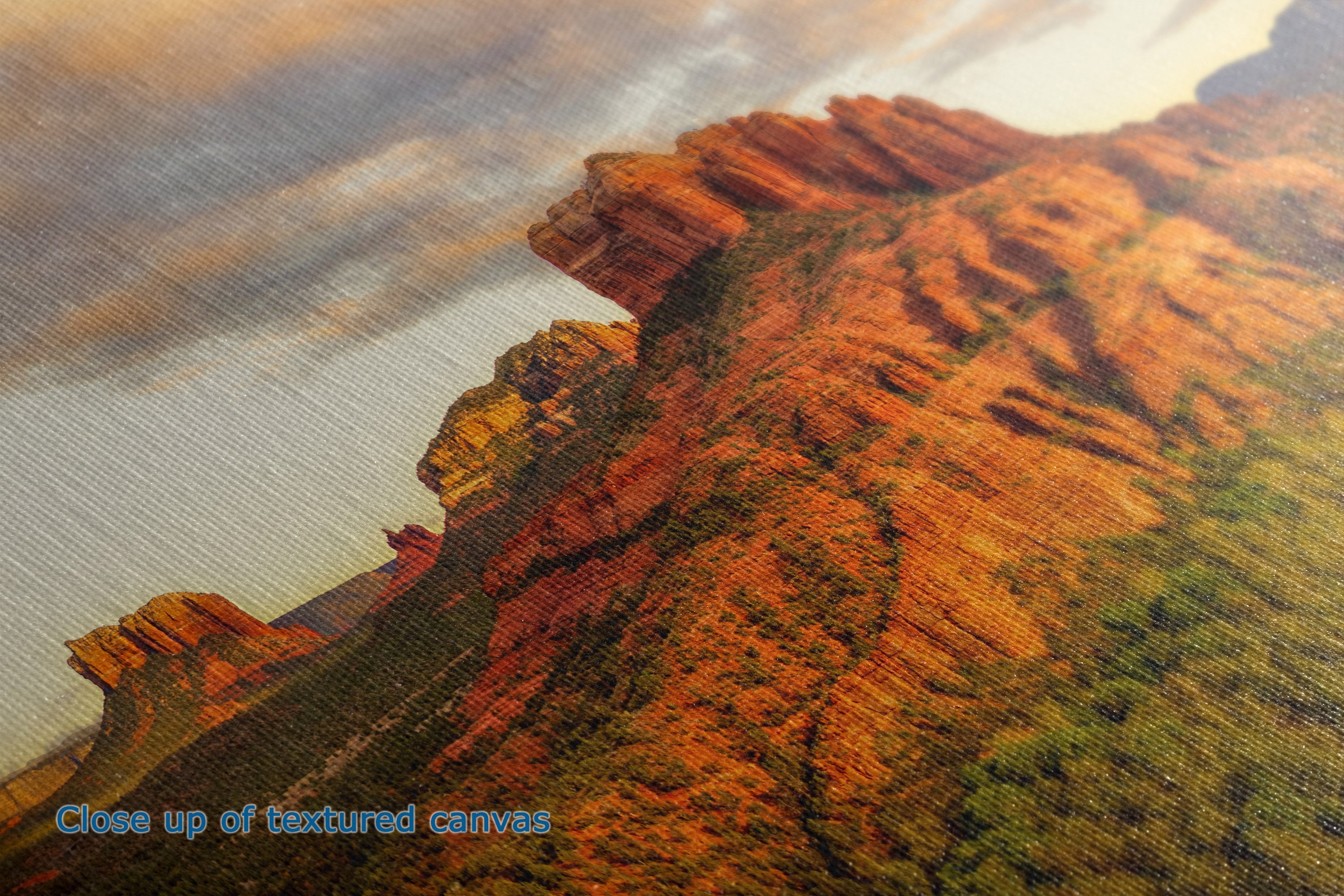 Close-up of the texture of a canvas print showing the detail of a desert canyon landscape with orange and red rock formations under a cloudy sky.