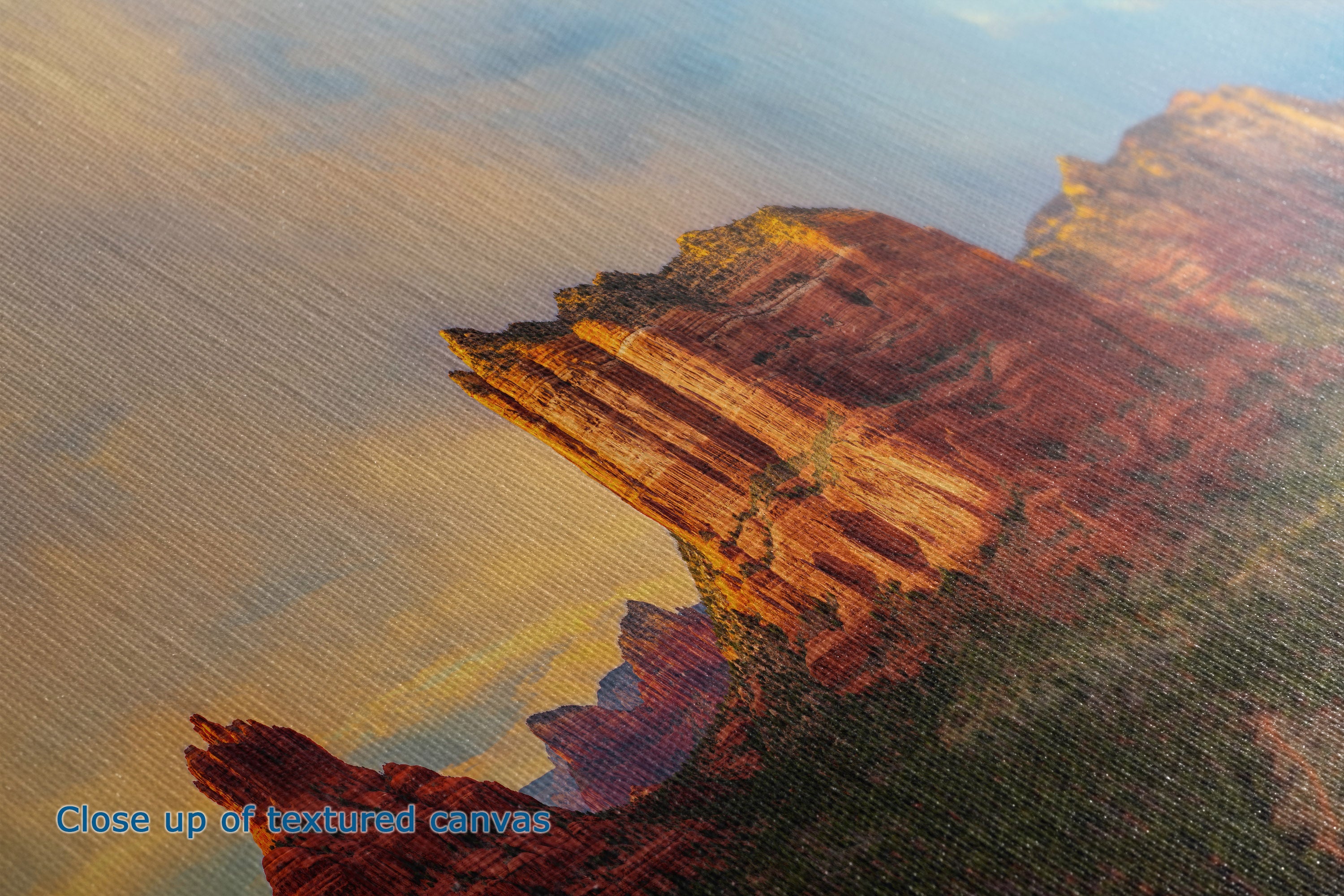 Close-up of a textured canvas print depicting a canyon landscape with layered red and orange rock formations under a warm sky.