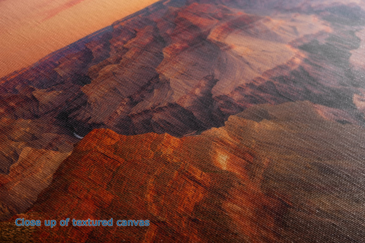 Close-up of a textured canvas print depicting a desert canyon landscape in warm orange, brown, and reddish tones, with blue text in the lower-left corner reading 'Close up of textured canvas'.