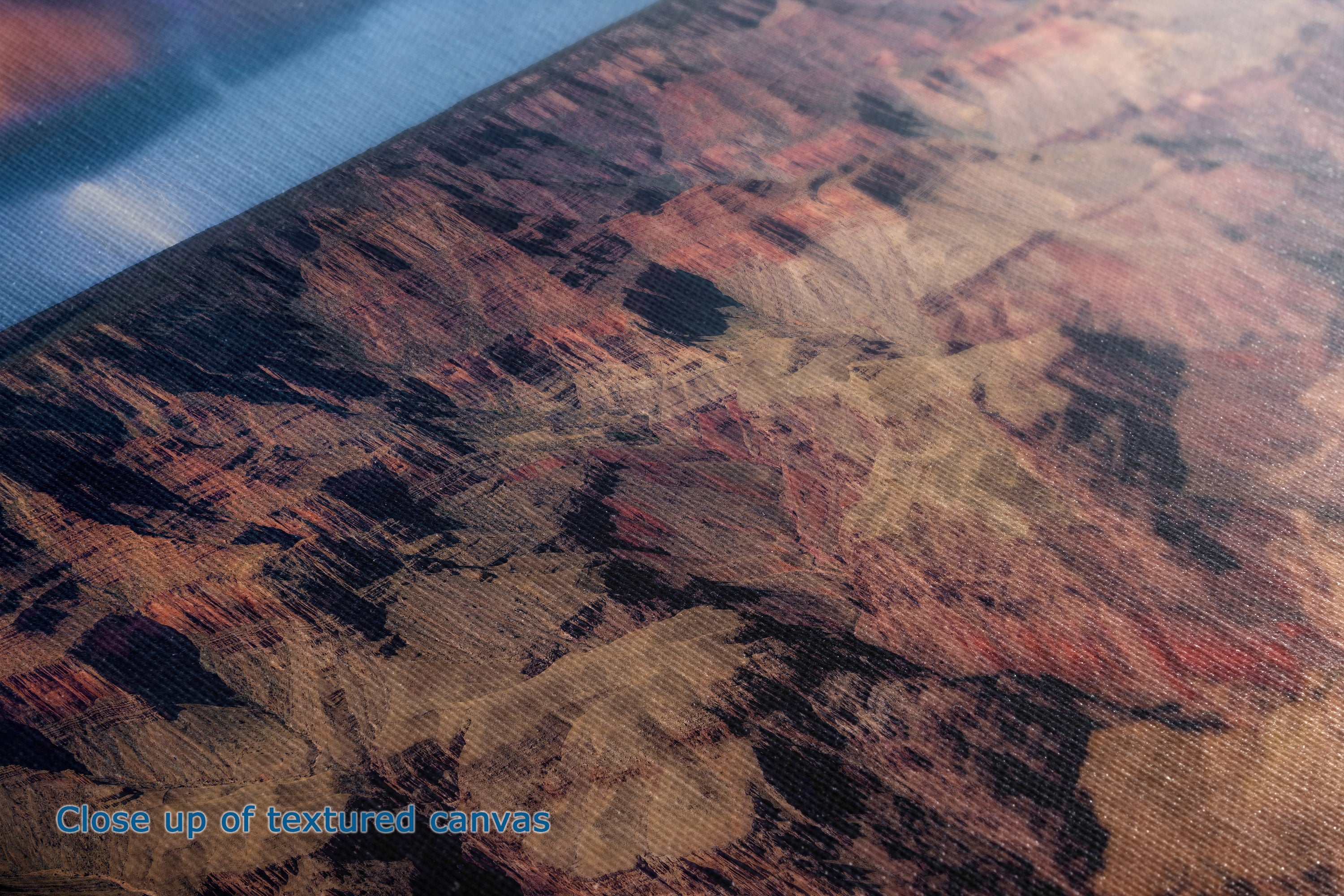 Close-up of a textured canvas print featuring a canyon landscape in earthy tones of brown, beige, and black, with a blue textured surface visible in the upper left corner.