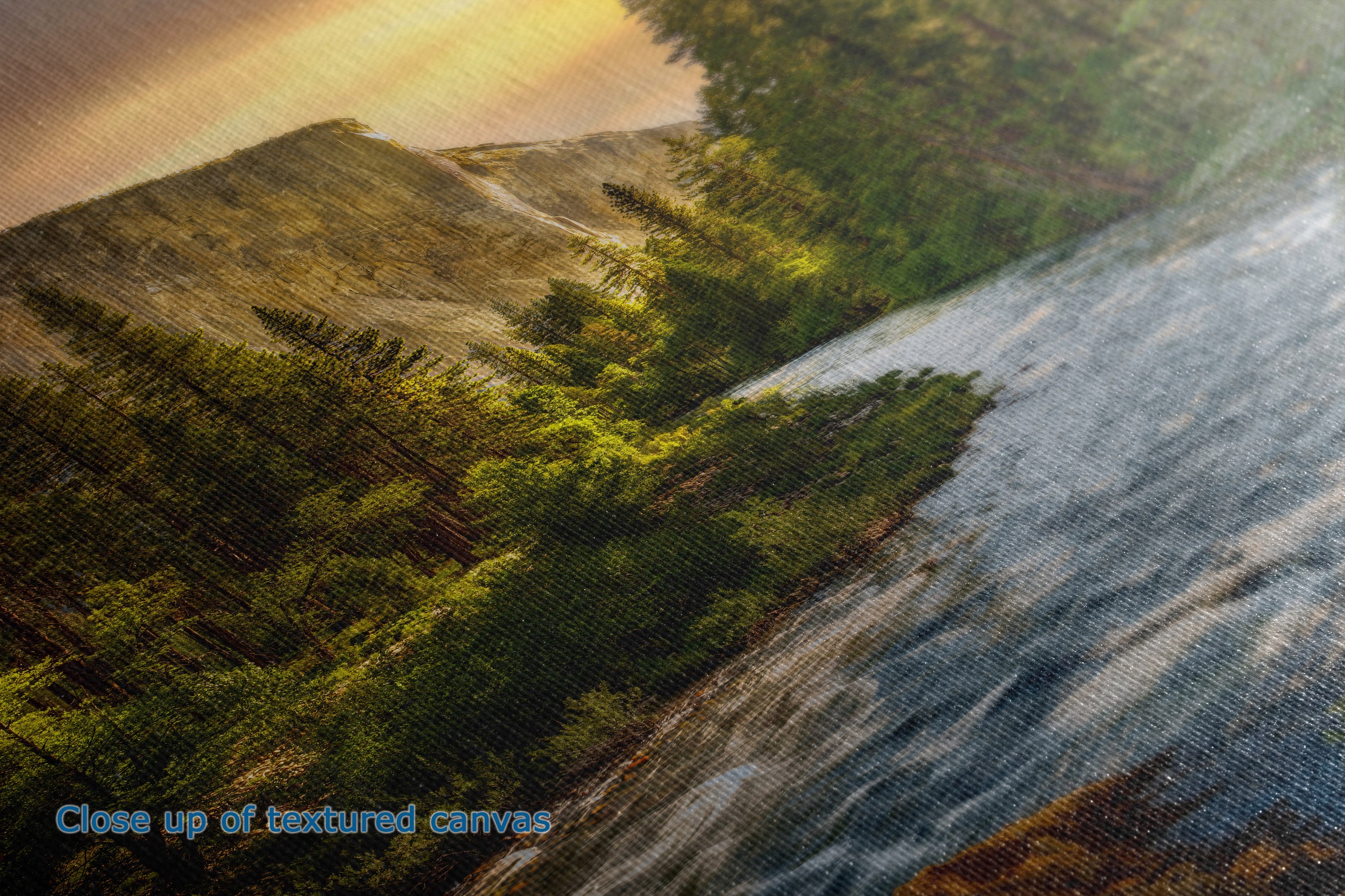 A close-up of the detail and texture of a canvas wall art print showing a forested hillside beside a flowing river under warm golden light.