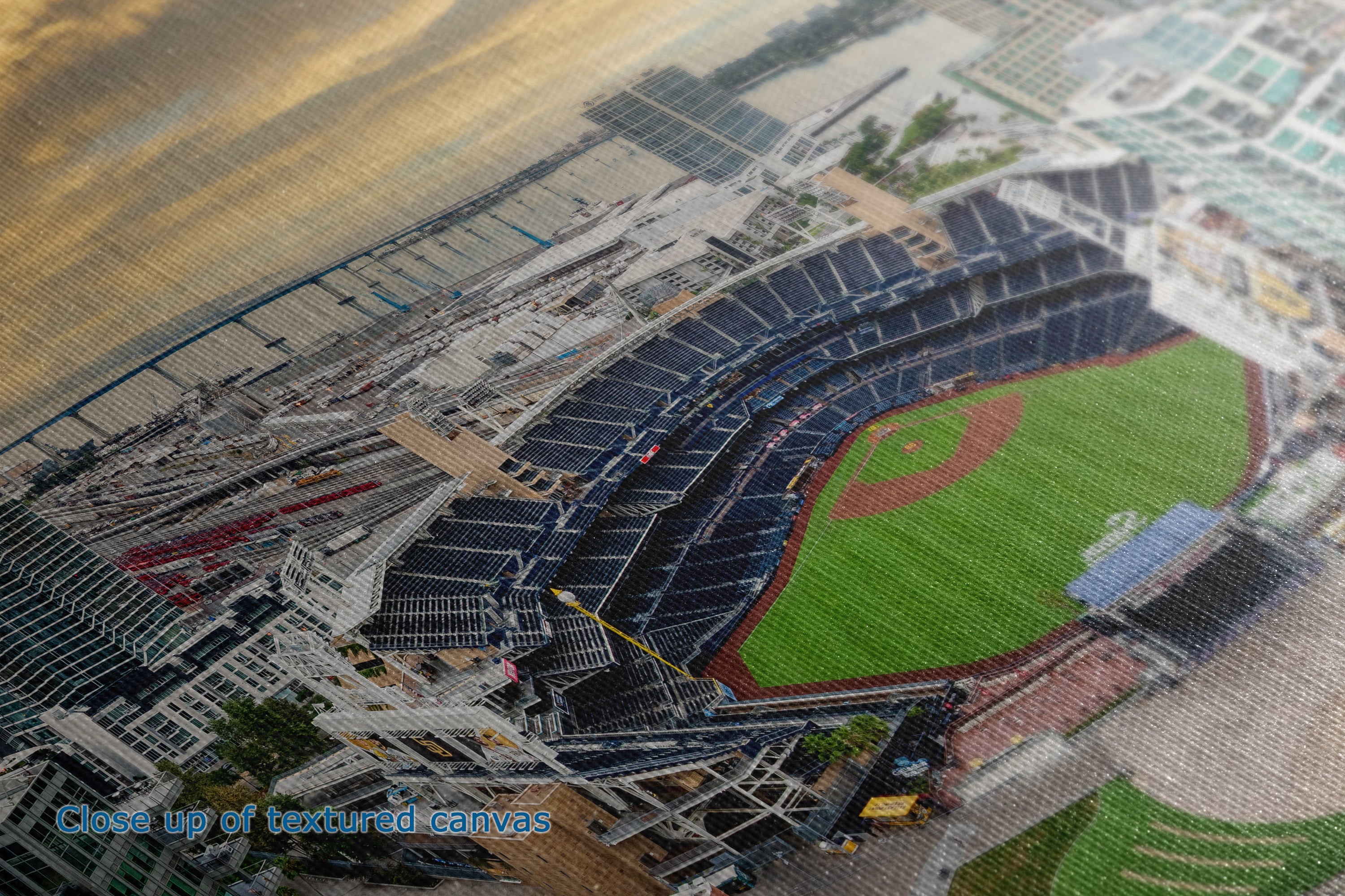 A close-up of a printed or textured baseball stadium scene, showing the field, stands, surrounding buildings, and sky in a detailed overhead view.