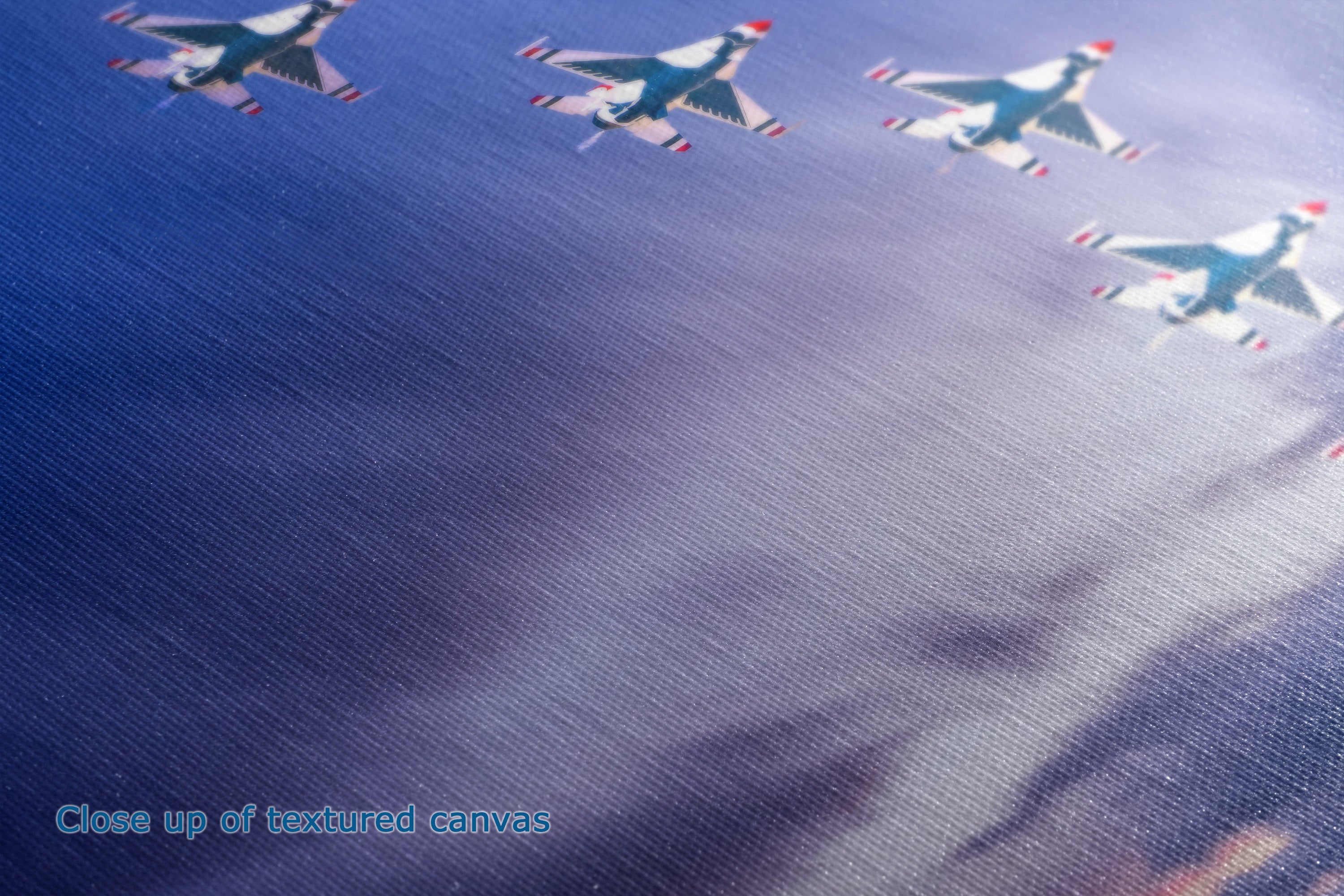 A Close-up detail and textured view of a canvas print depicting fighter jets flying in formation against a blue sky with soft light rays.