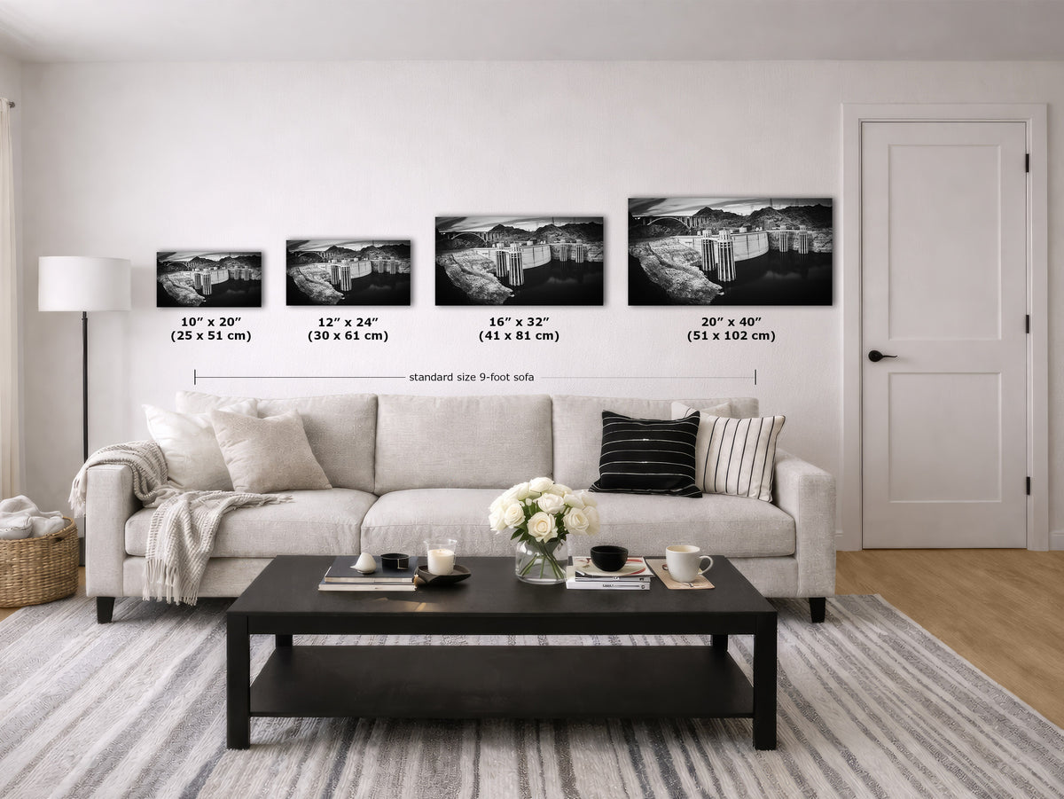 A staged living room showing four framed black-and-white landscape wall art prints above a light sofa, with size labels and measurements for each print size. The room includes a coffee table, lamp, rug, basket, and door.