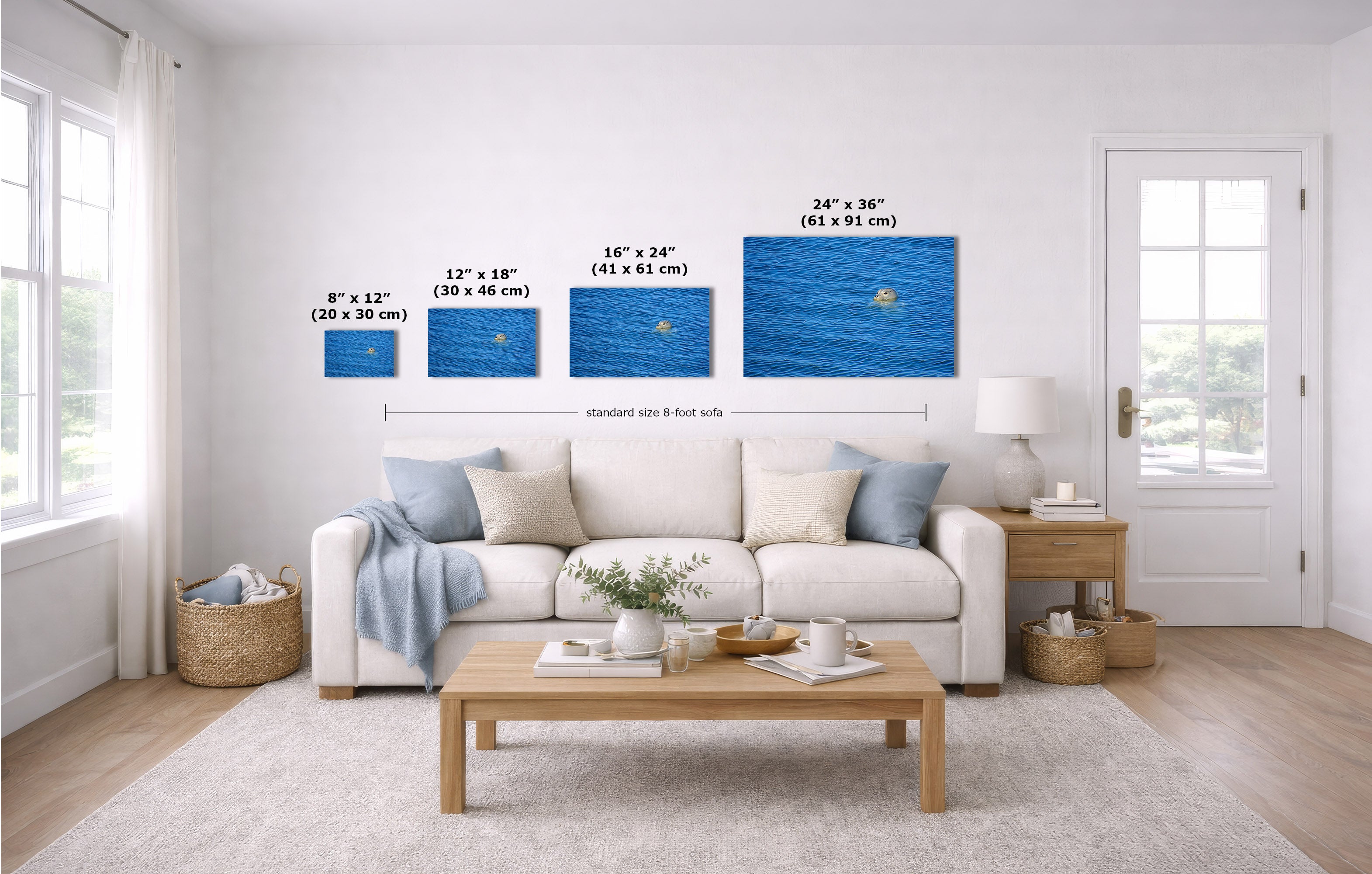 A staged living room shows a white sofa, coffee table, side table, rug, and wall art. The product being highlighted is a set of four blue ocean-style canvas prints mounted on the wall, each labeled with dimensions in inches and centimeters.