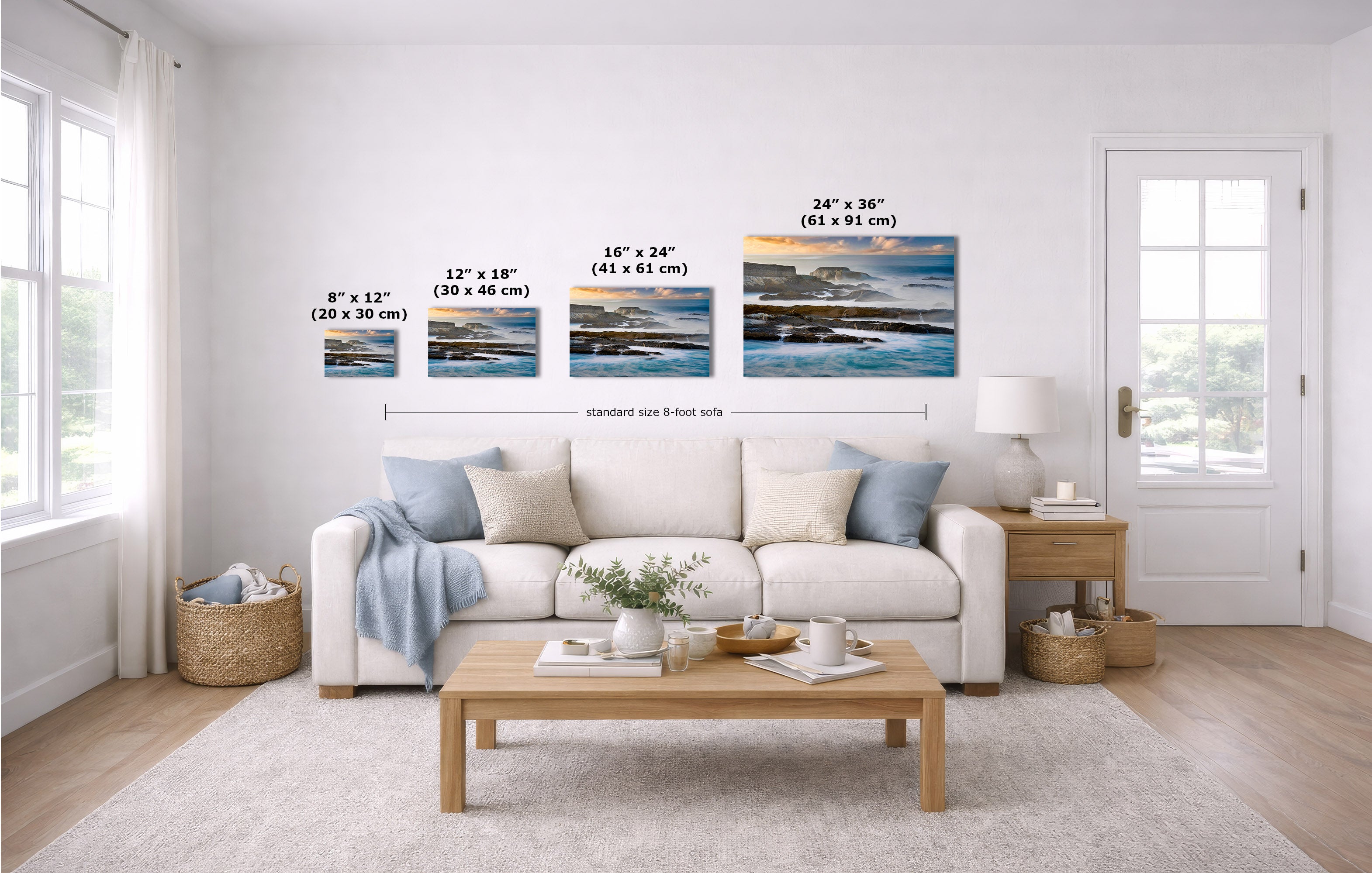 A staged living room with a white sofa, coffee table, and wall-mounted framed art. The product being shown is the set of four horizontal landscape prints above the couch, with size labels overlaid in inches and centimeters.