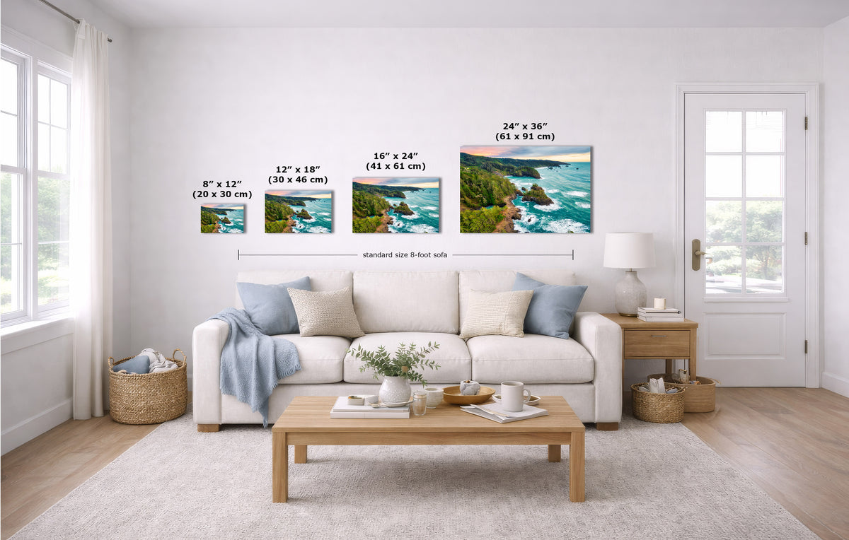 A staged living room with a white sofa, coffee table, and wall-mounted coastal landscape prints. Black measurement lines and text labels show the dimensions of four wall art sizes relative to an 8-foot wall.
