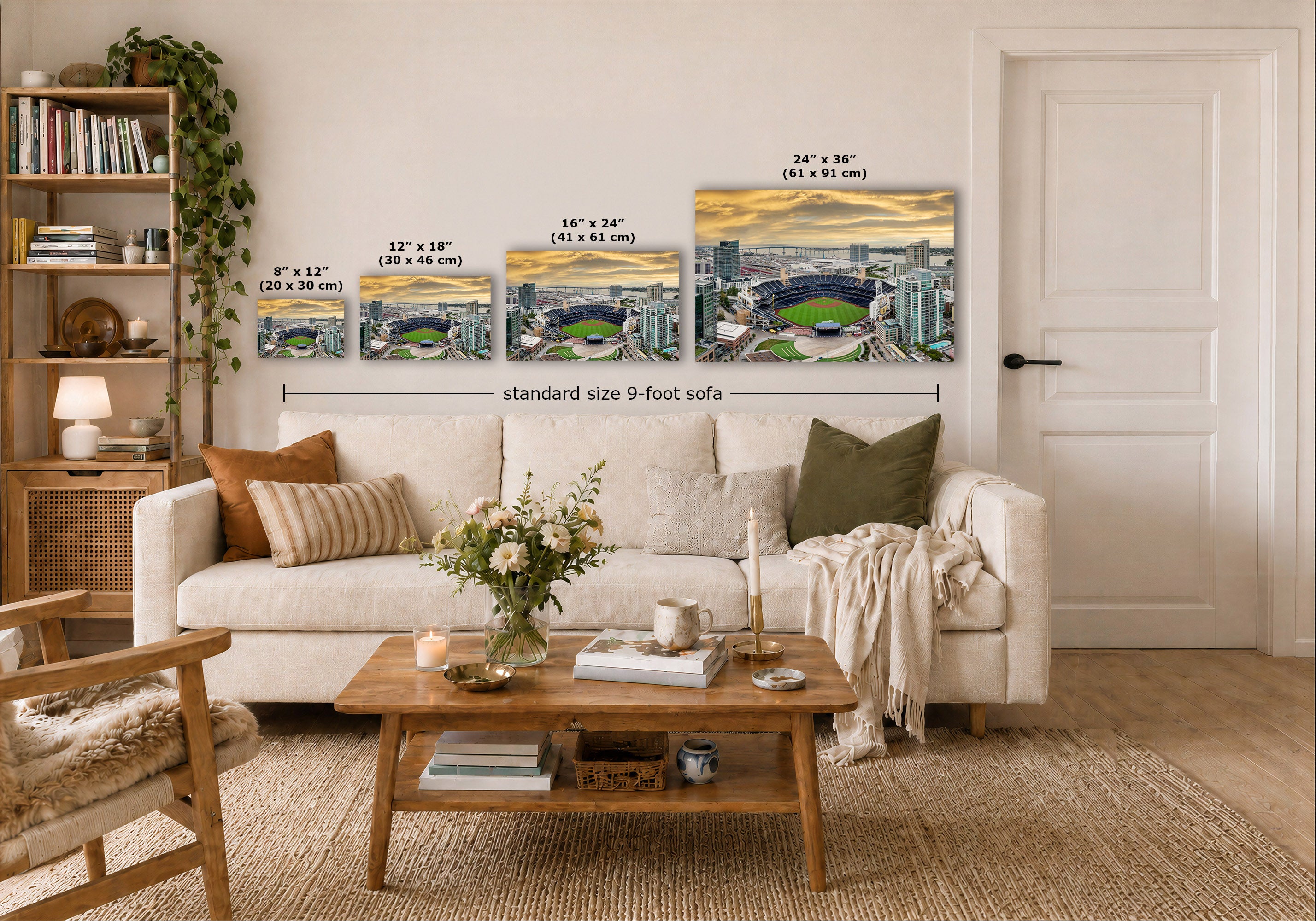 Three cityscape wall art prints are displayed above a white sofa in a styled living room. The prints show stadium scenes with overlaid size labels: 8 x 12, 12 x 18, 16 x 24, and 24 x 36, plus a dimension line reading standard size 9-foot sofa.
