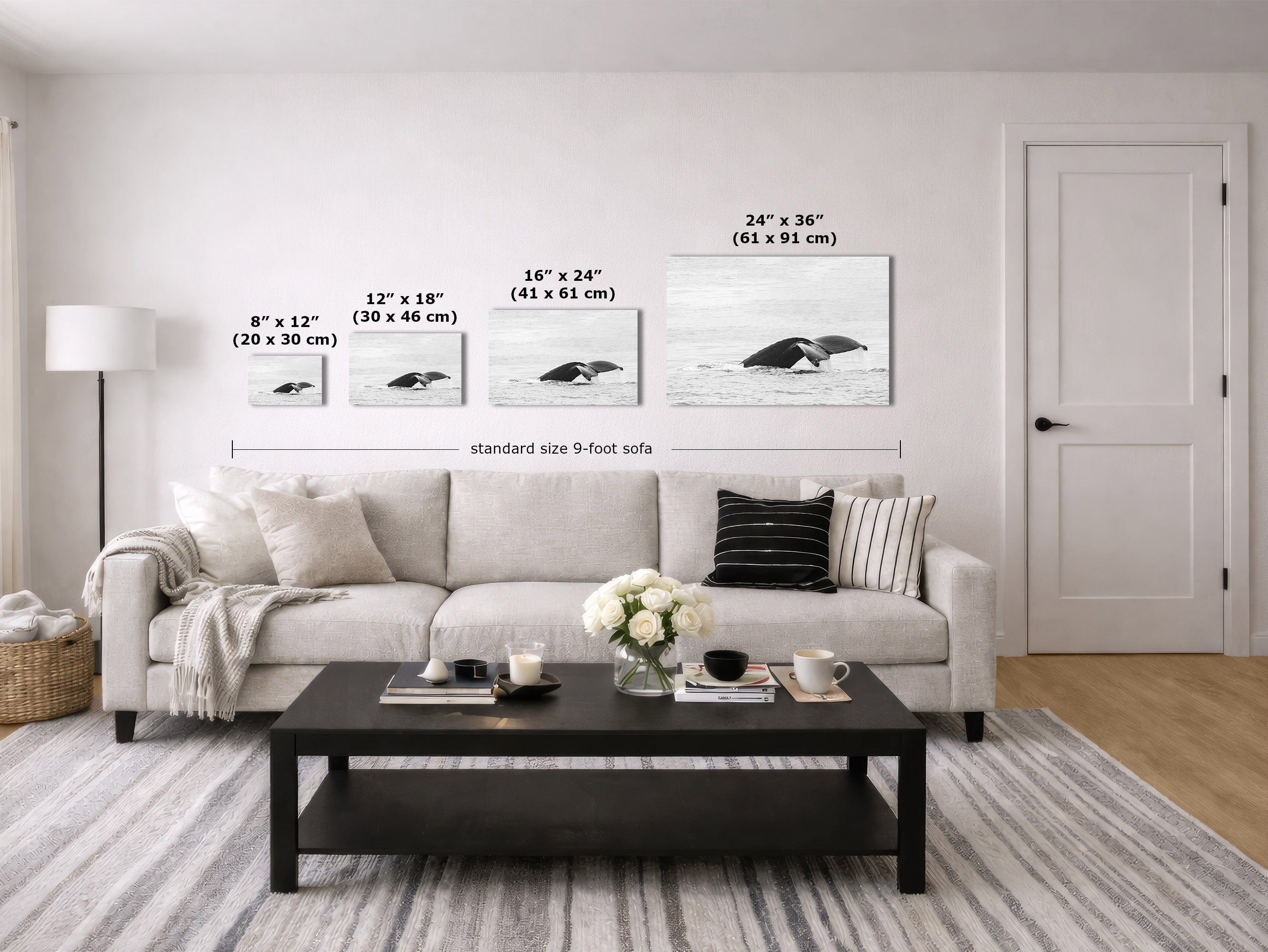 A staged living room showing four whale art prints mounted on a light wall above a sofa, with size labels and measurements printed on the image. The room includes a light gray sofa, black coffee table, rug, floor lamp, and a white door.