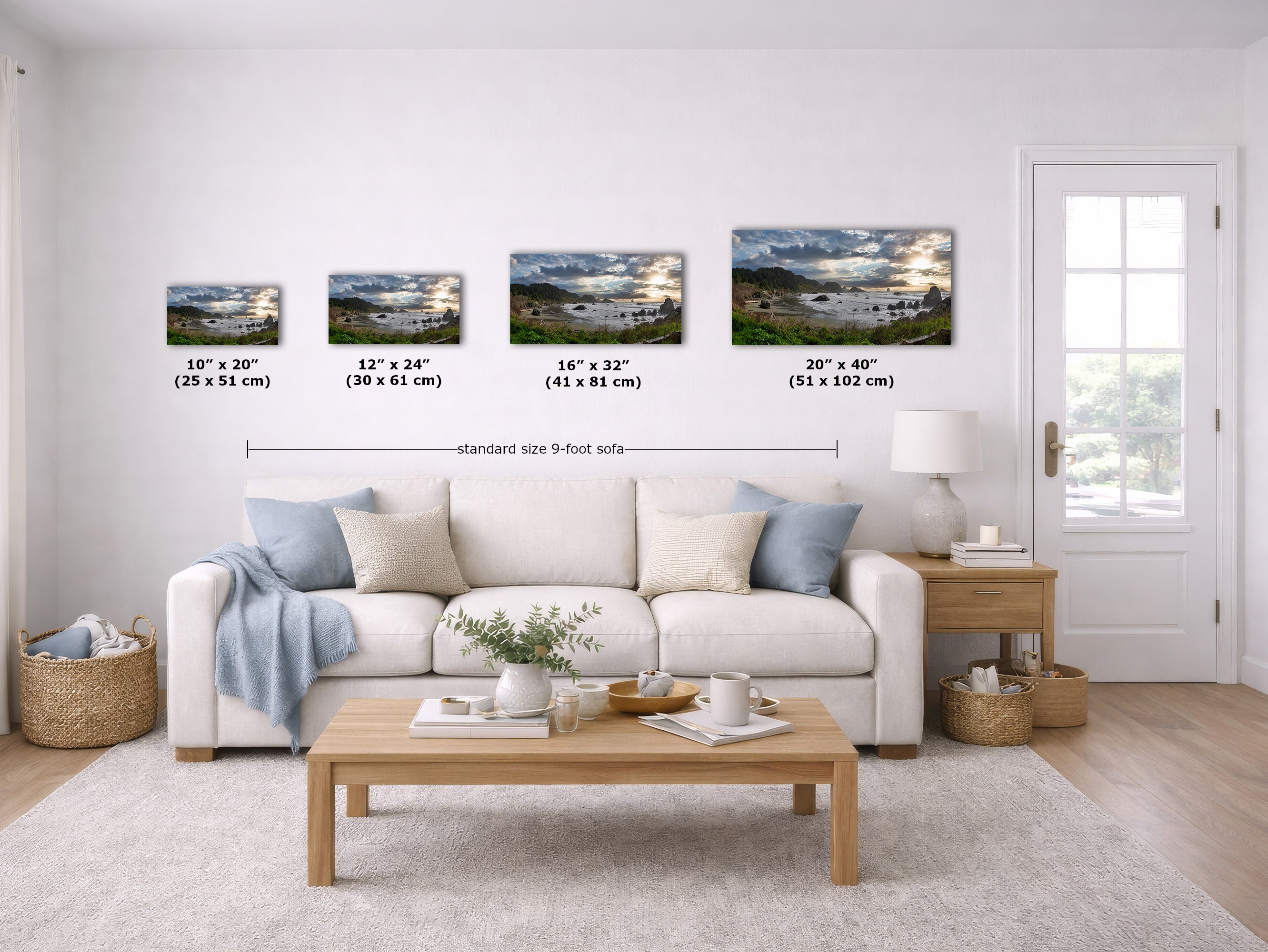 A staged living room showing four landscape wall art prints above a white sofa, with size labels for each print. The scene includes a coffee table, side table, lamp, baskets, and a glass door, and the prints depict scenic lake and mountain landscapes.