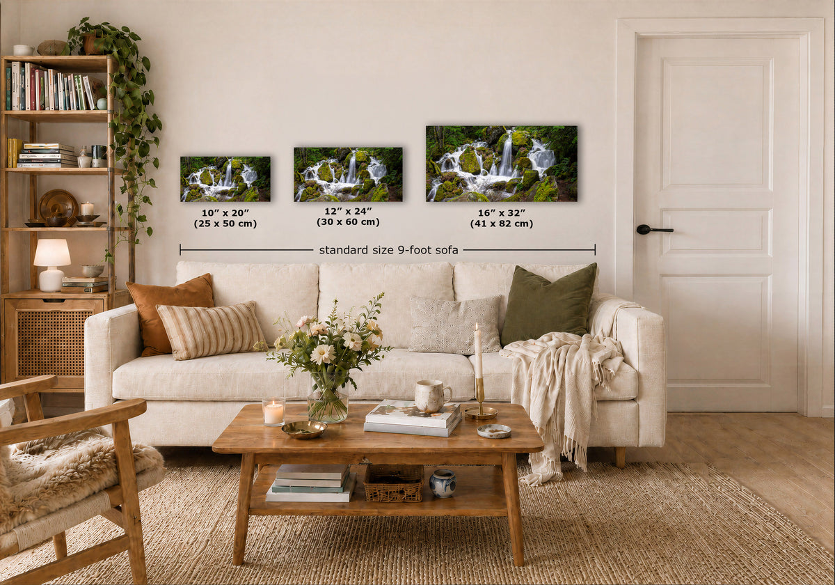 Three wall art prints showing waterfall scenes are displayed above a white sofa in a styled living room. White text labels indicate the dimensions of each print: 10" x 20" (25 x 50 cm), 12" x 24" (30 x 60 cm), and 16" x 32" (41 x 82 cm), with a dimension line reading 'standard size 9-foot sofa'.