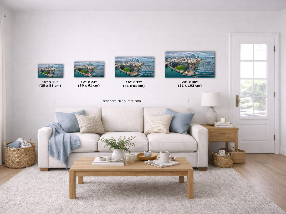 A staged living room shows a white sofa, coffee table, side table, rug, and a set of four wall art prints above the couch. The prints depict a coastal harbor scene with ships and blue water, with size labels beneath each print and a line indicating standard size 9-foot sofa spacing.