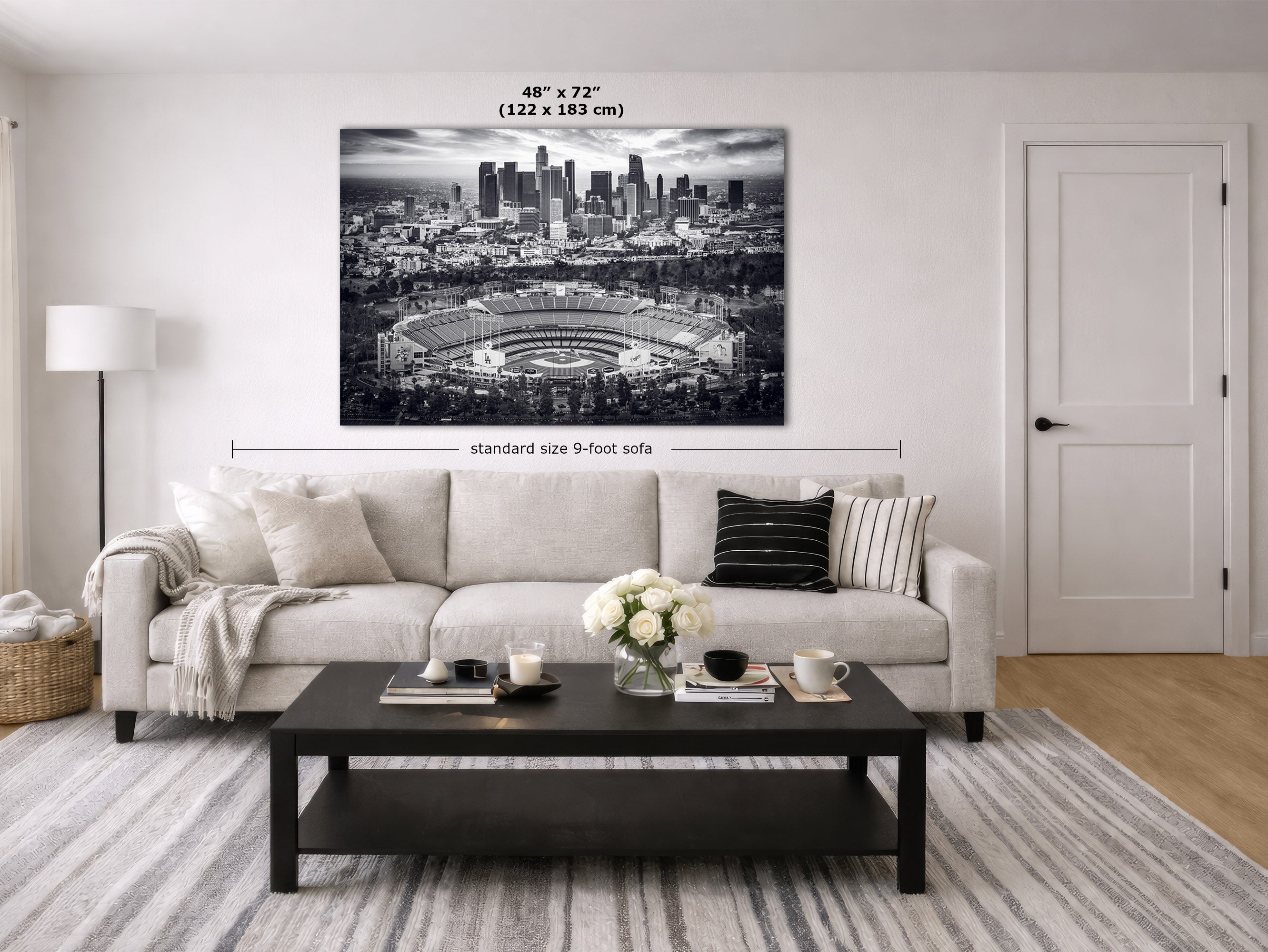 A large black and white Los Angeles Dodgers Stadium Artwork canvas print hangs on a white wall in a modern living room mockup. The image includes dimension overlays indicating the canvas is 48 inches by 72 inches (122 x 183 cm) and shows a sofa below for scale.
