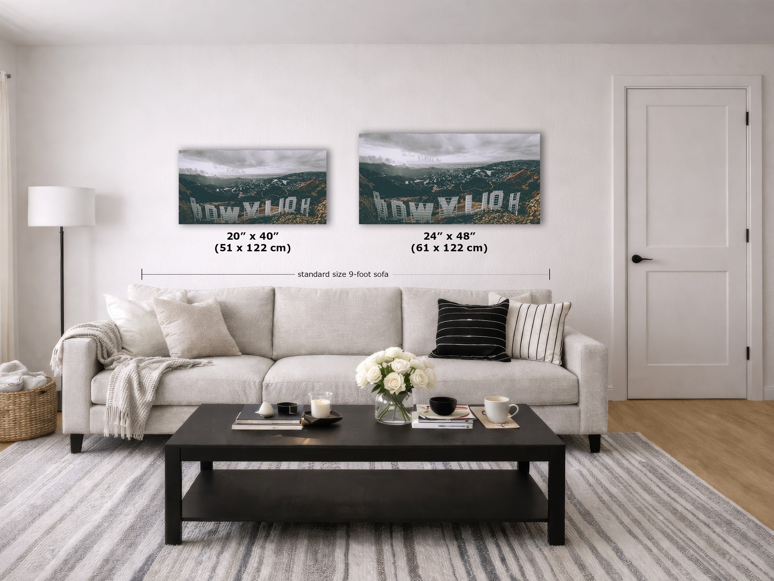 A staged living room shows a white sofa with pillows, a black coffee table, a rug, and two framed wall art prints above the couch. The prints depict a mountain landscape.