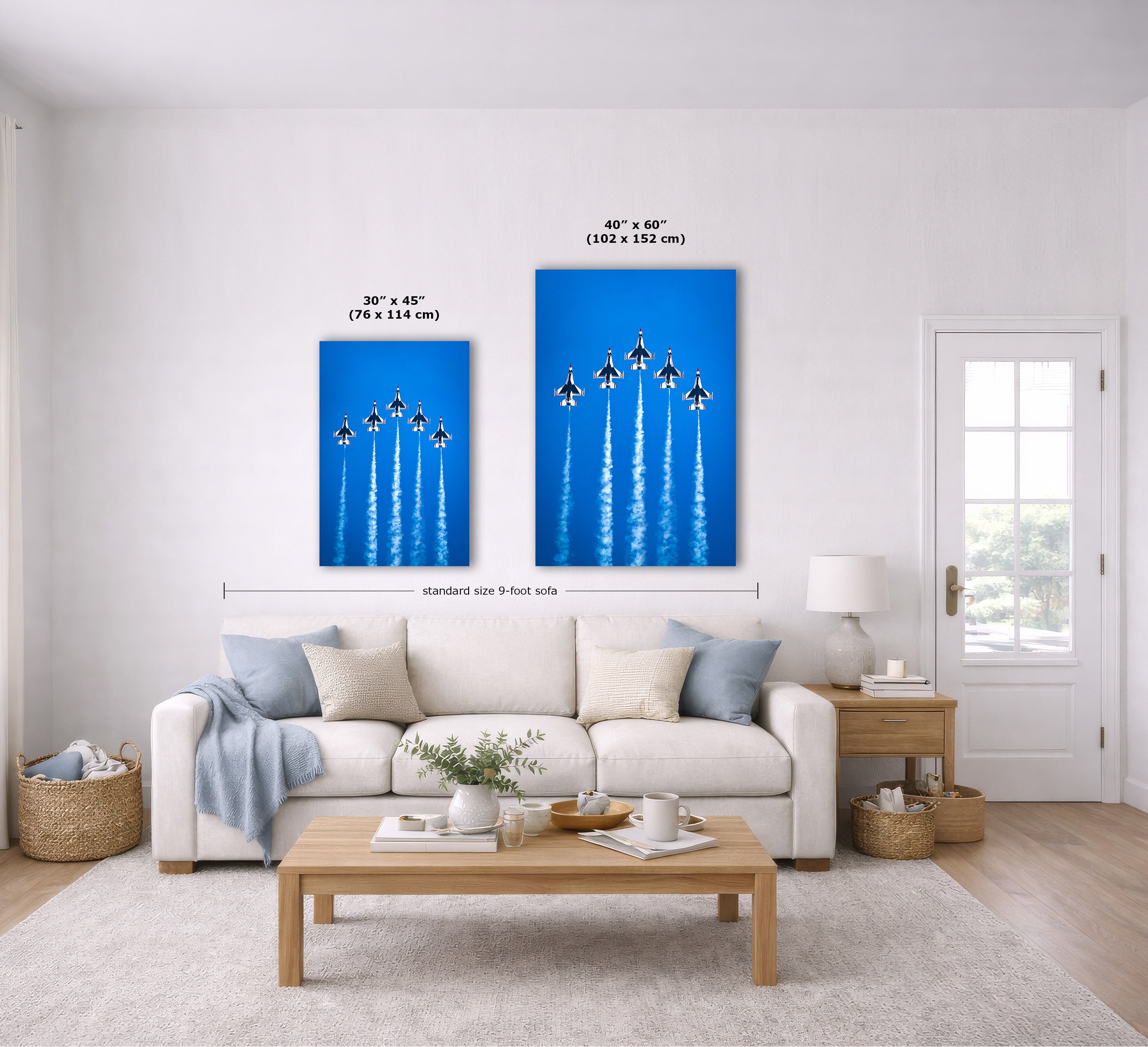 Two blue wall art prints showing jet aircraft formations are displayed above a white sofa in a bright living room. Black measurement lines and text indicate the dimensions of the two prints: 30 x 45 inches (76 x 114 cm) and 40 x 60 inches (102 x 152 cm).