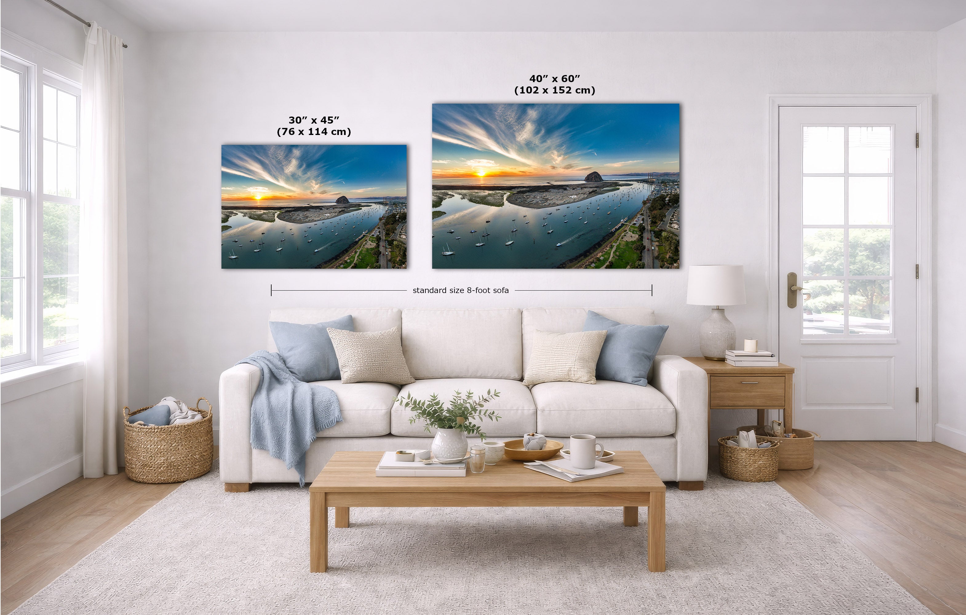 A staged living room with a white sofa, coffee table, and two landscape wall art prints above the couch. The prints show a coastal sunset scene with blue water and warm sky tones, with size labels and dimension lines overlaid.