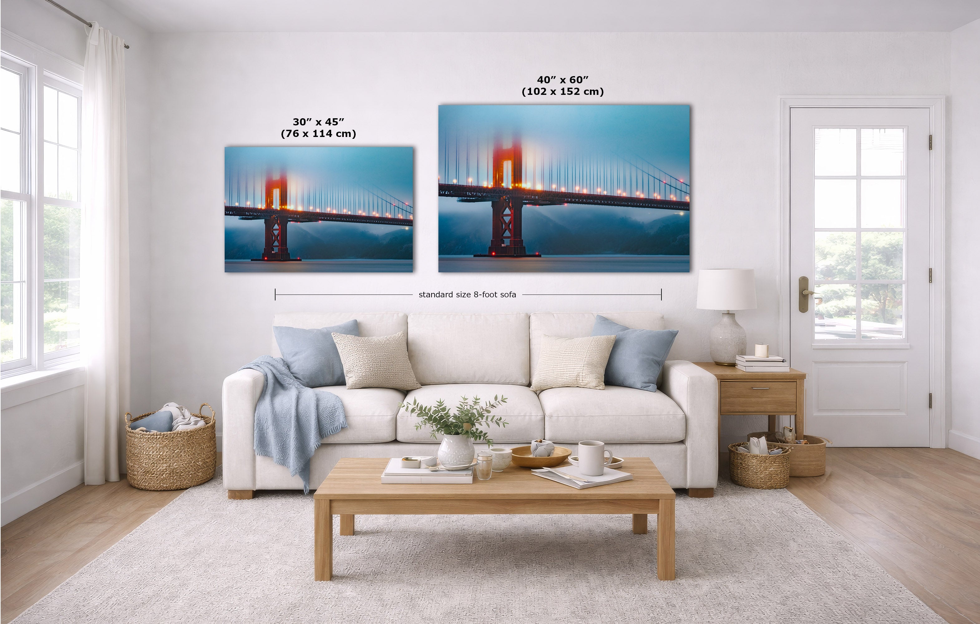 A staged living room with a white sofa, coffee table, and wall art showing two versions of a bridge print with size labels: 30 x 45 inches and 40 x 60 inches. The room is bright and clean, with a white door, windows, and light wood flooring.